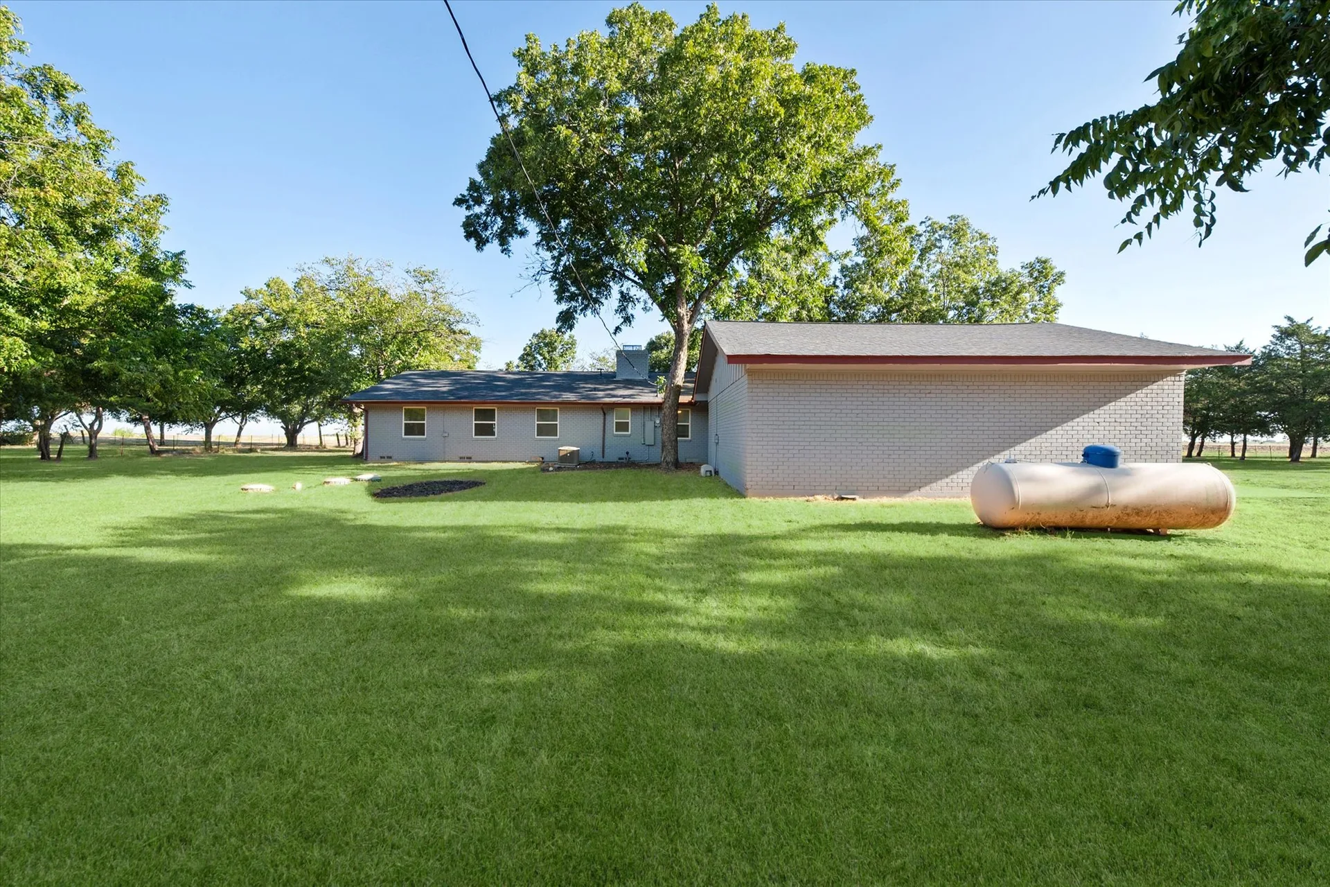 Rear exterior of the ranch home with a large grassy yard and mature trees