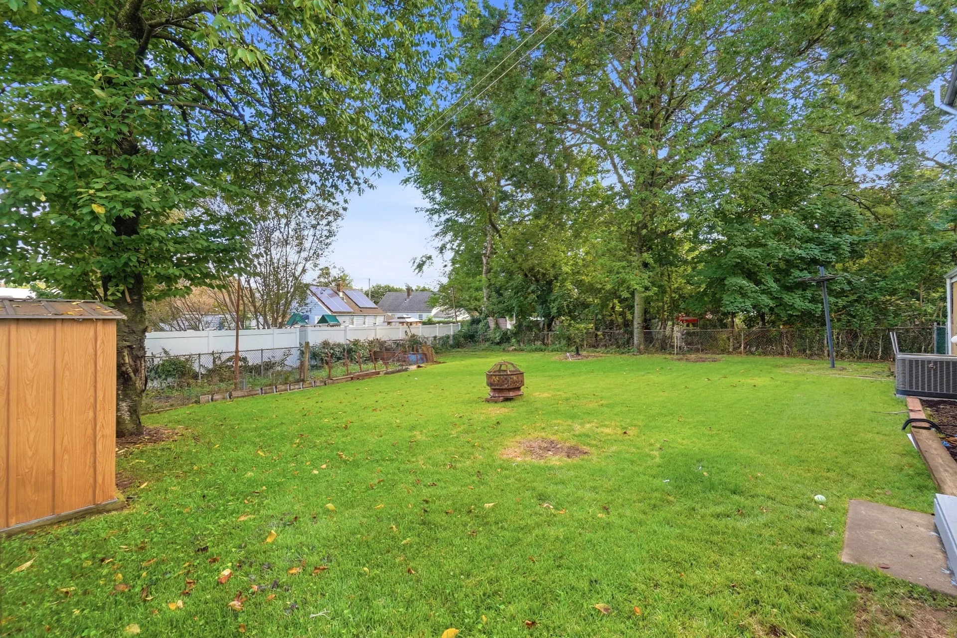 Backyard lawn with mature trees, a wood storage shed, and white vinyl fencing