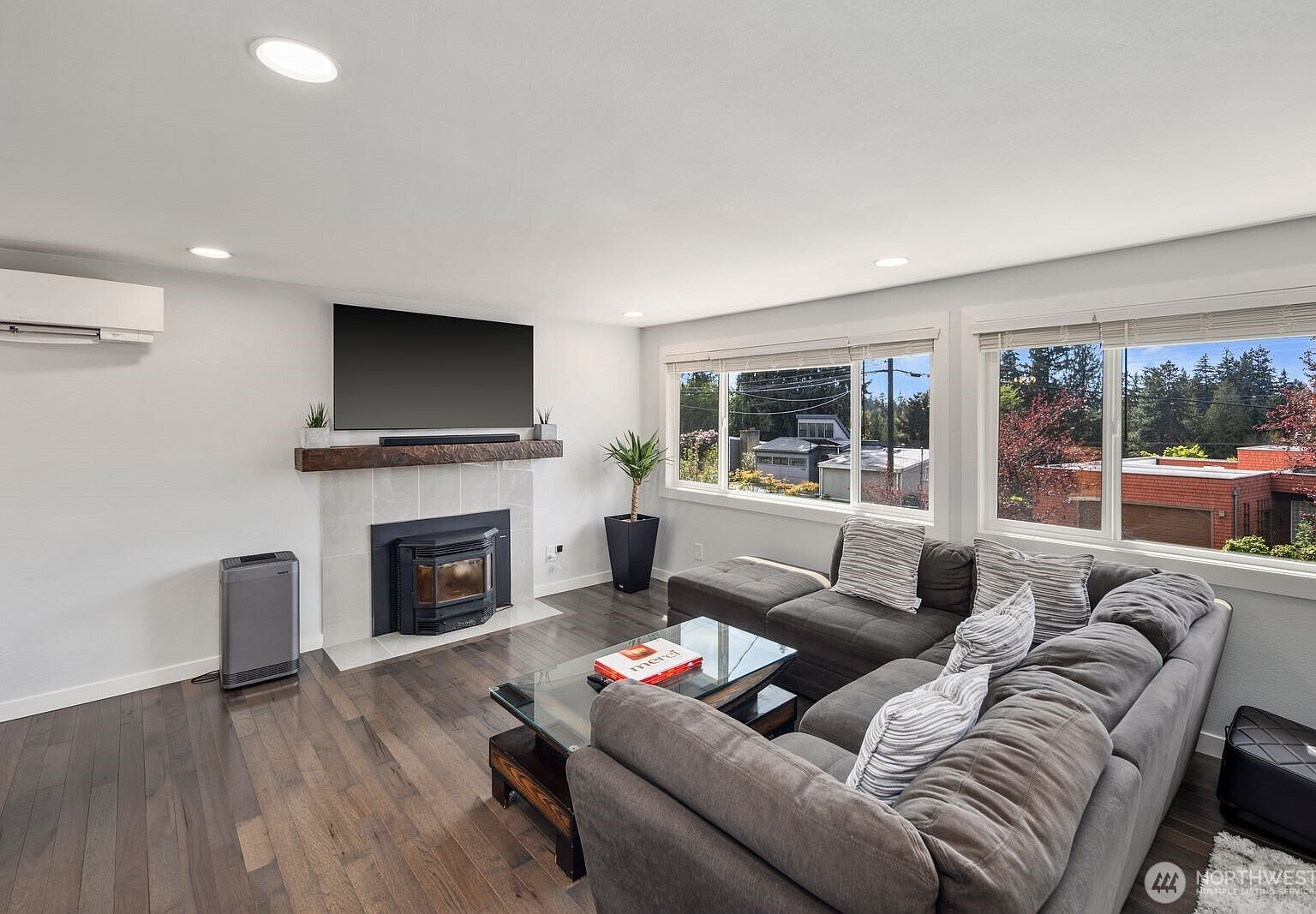 Living room with dark hardwood floors, stone tile fireplace, and large double-pane windows