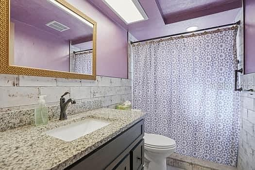 Second bathroom with granite vanity, subway tile, and purple walls