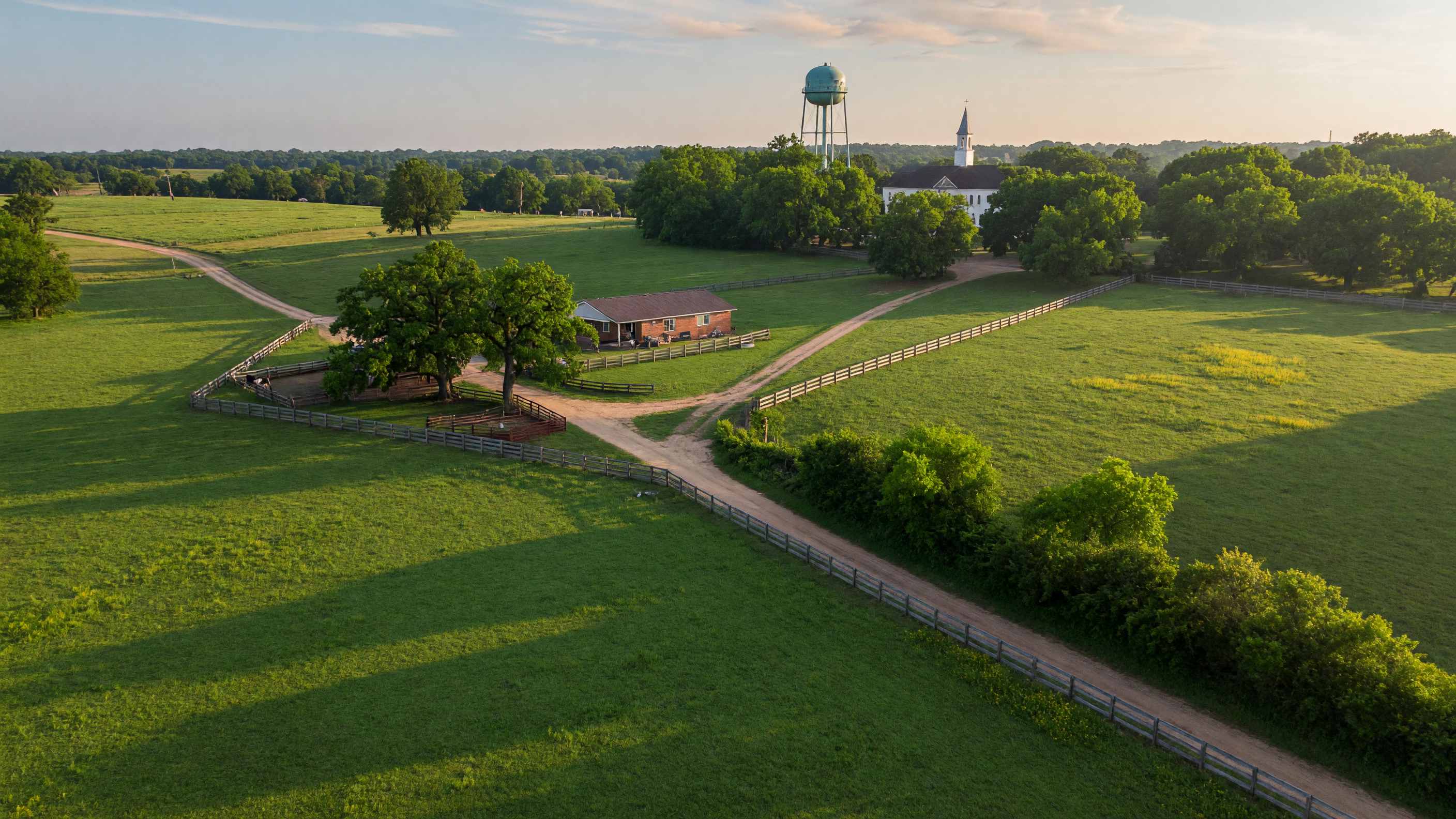 Rolling green pastures and tree-lined rural roads in Northeast Texas with a small-town water tower visible on the horizon under a bright summer sky