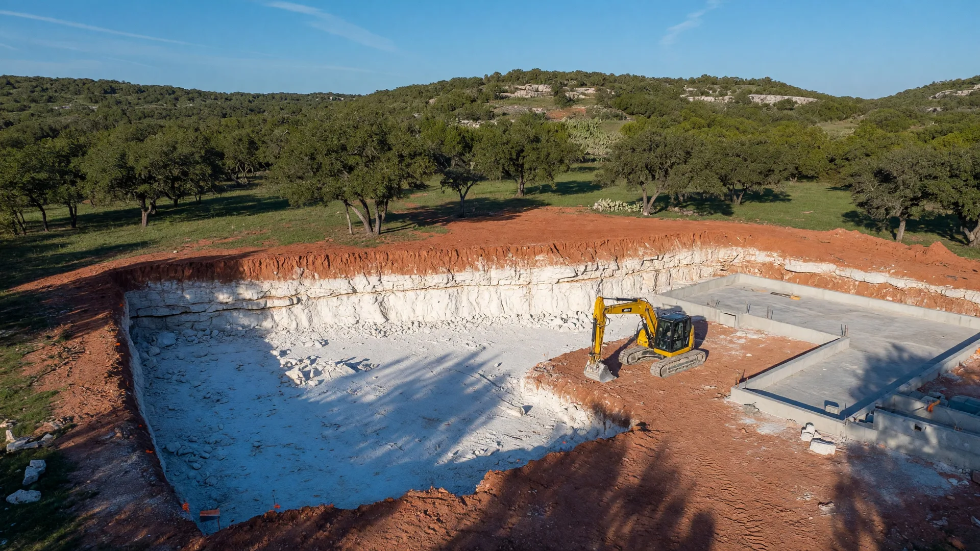 Aerial view of a Texas Hill Country excavation site showing exposed caliche and limestone layers beneath topsoil during foundation work