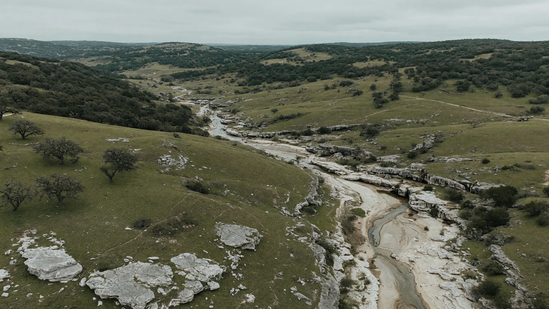Aerial view of the Texas Hill Country landscape with rolling limestone hills and a winding creek bed, illustrating the terrain that shapes flood zones in the Boerne and Fair Oaks Ranch area