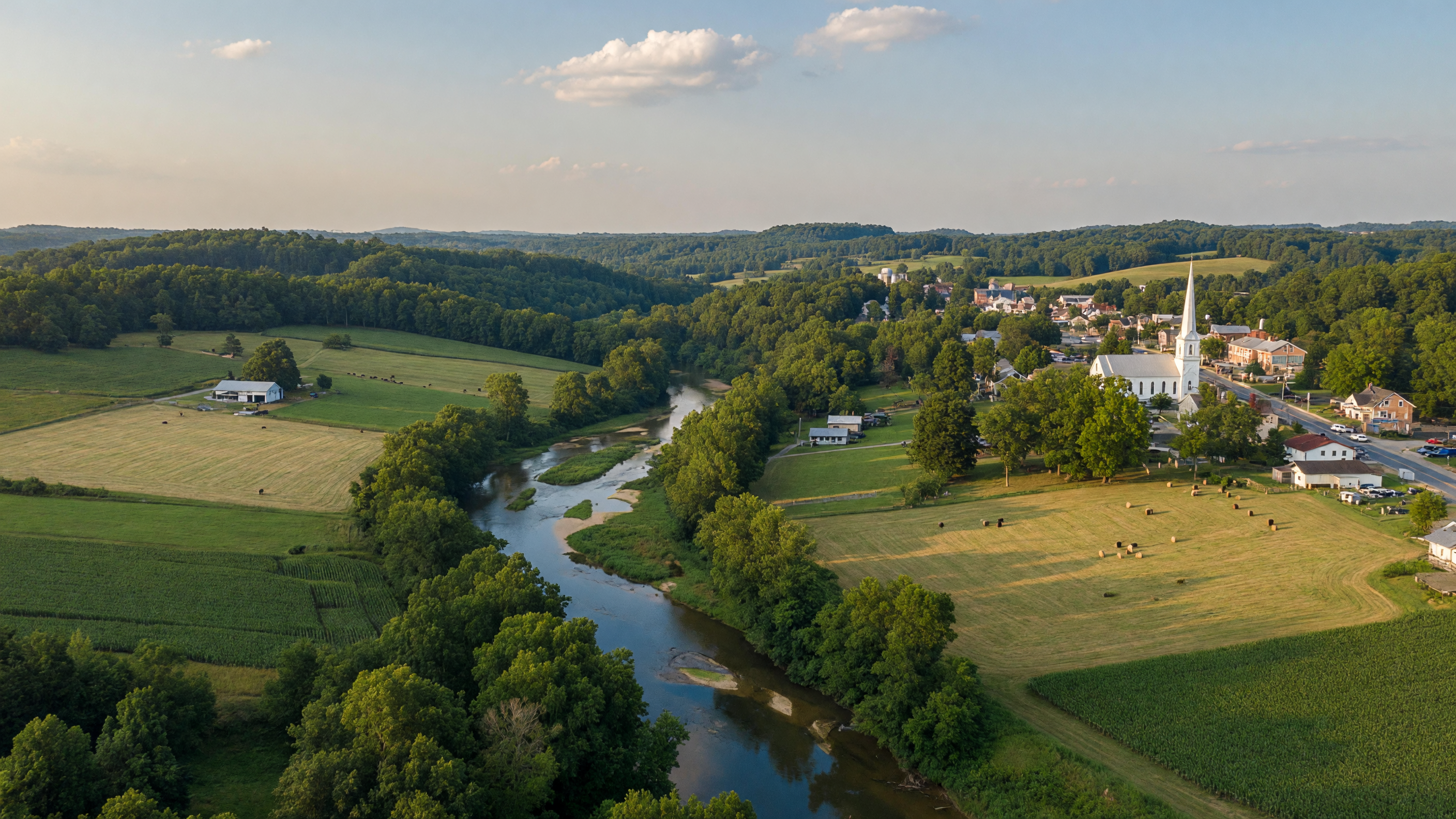 Rolling green Virginia countryside with farm fields, tree canopy, and a winding river in the golden afternoon light