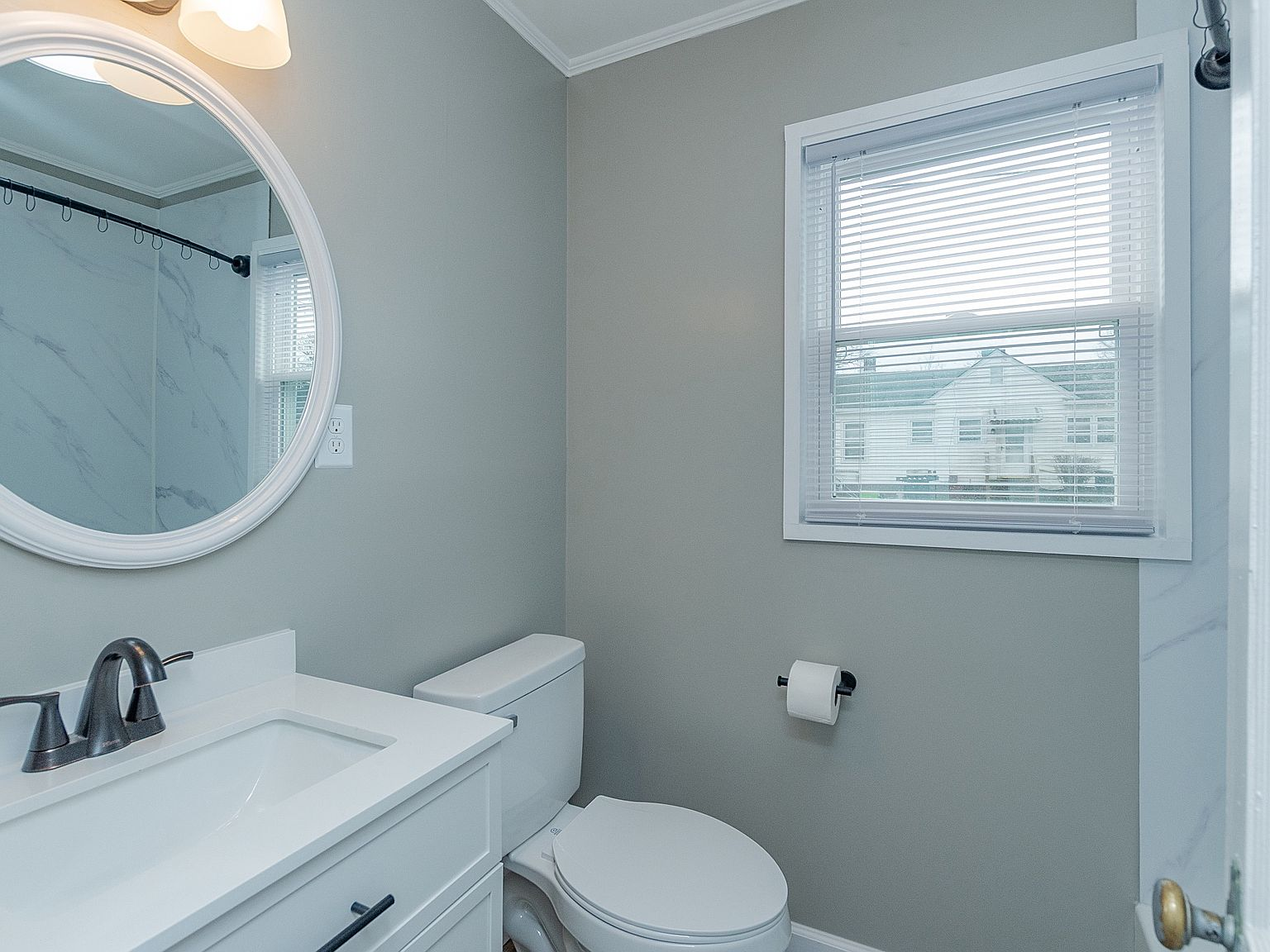 Modern renovated bathroom complete with white vanity, black hardware, and circular wall mirror