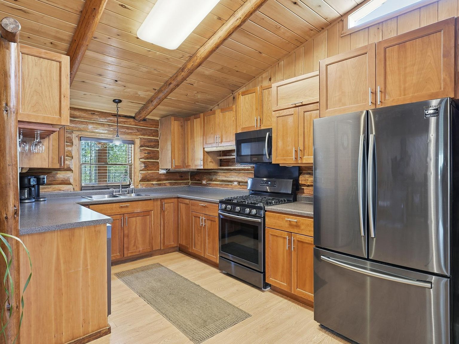 Kitchen with natural wood cabinets, log walls, and vaulted ceiling