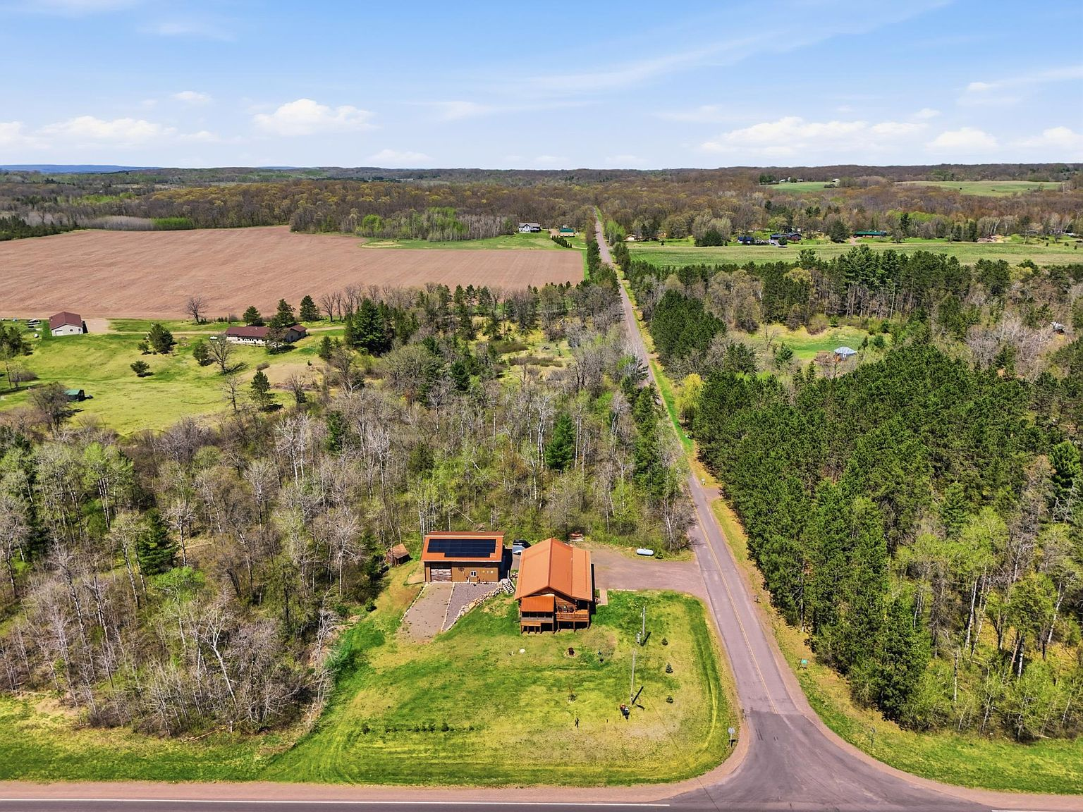 High drone aerial of property, garage with solar panels, and dense forest