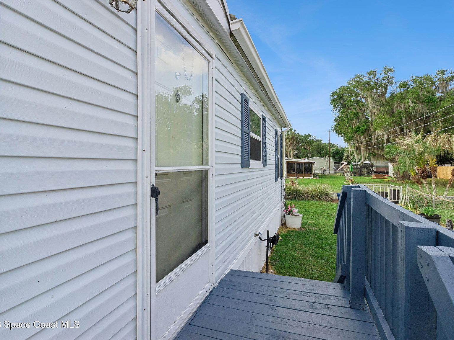 Side exterior view showing entrance with blue shutters and grey wooden deck