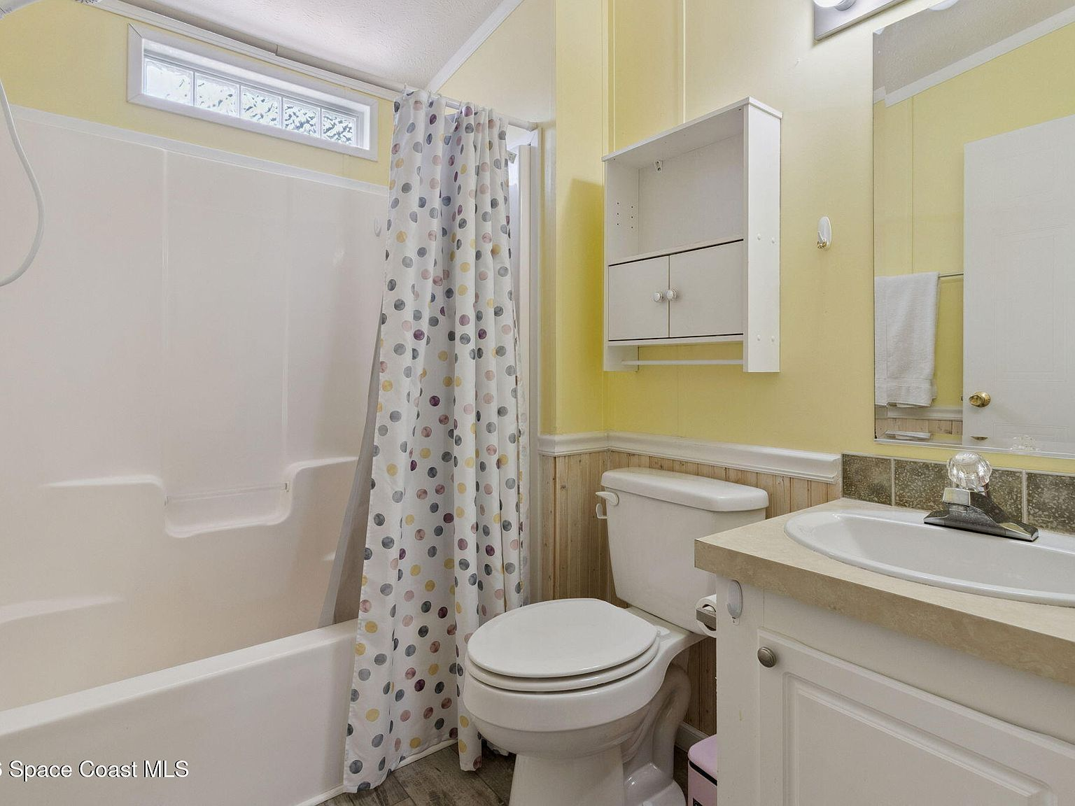 Bathroom with yellow paint, beadboard wainscoting, and white fiberglass tub