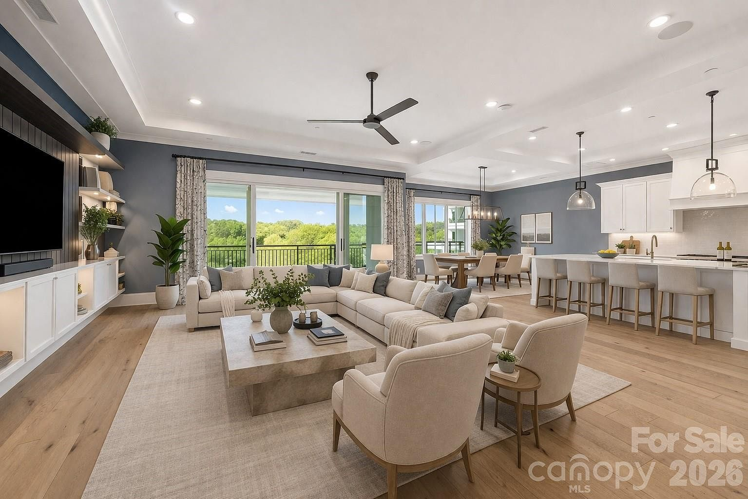 Open-concept living room with tray ceilings, light wood floors, and floor-to-ceiling sliding glass doors