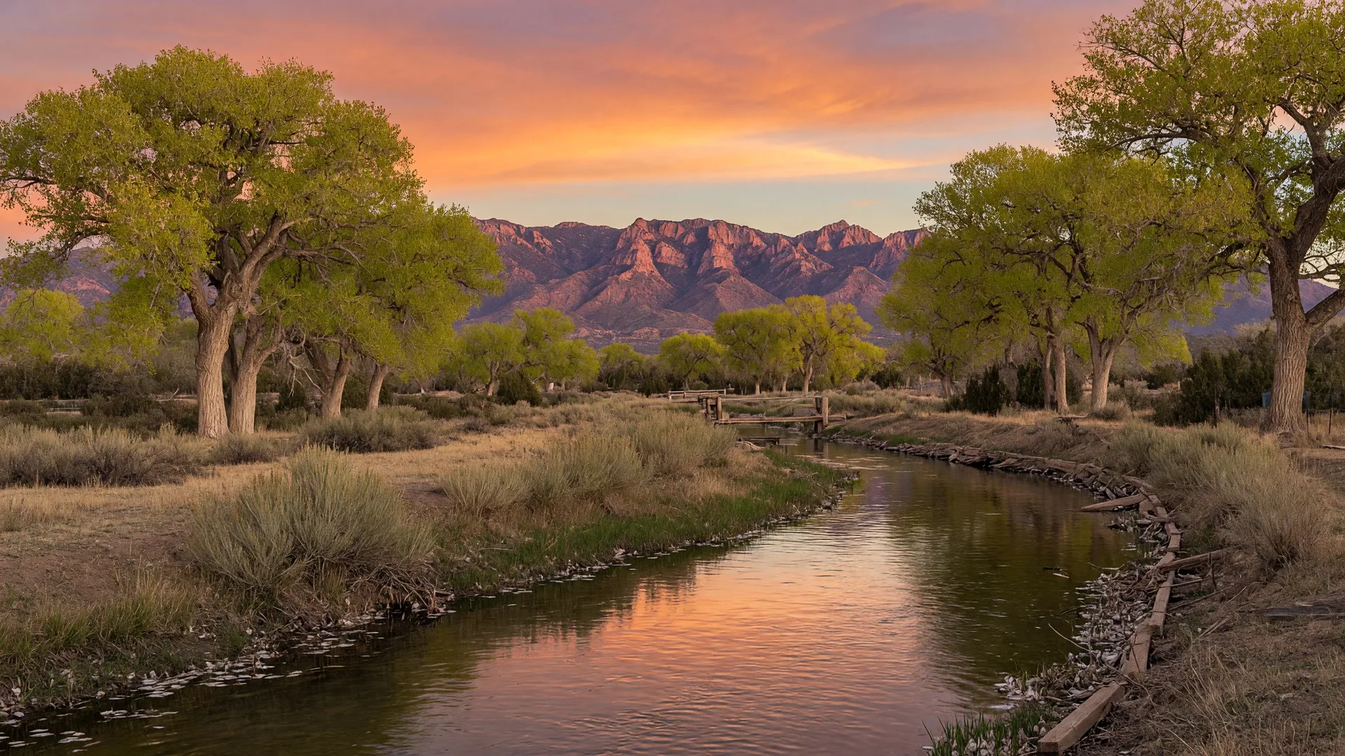 Acequia irrigation channel flowing through a New Mexico desert landscape at golden hour with Sandia Mountains in the distance