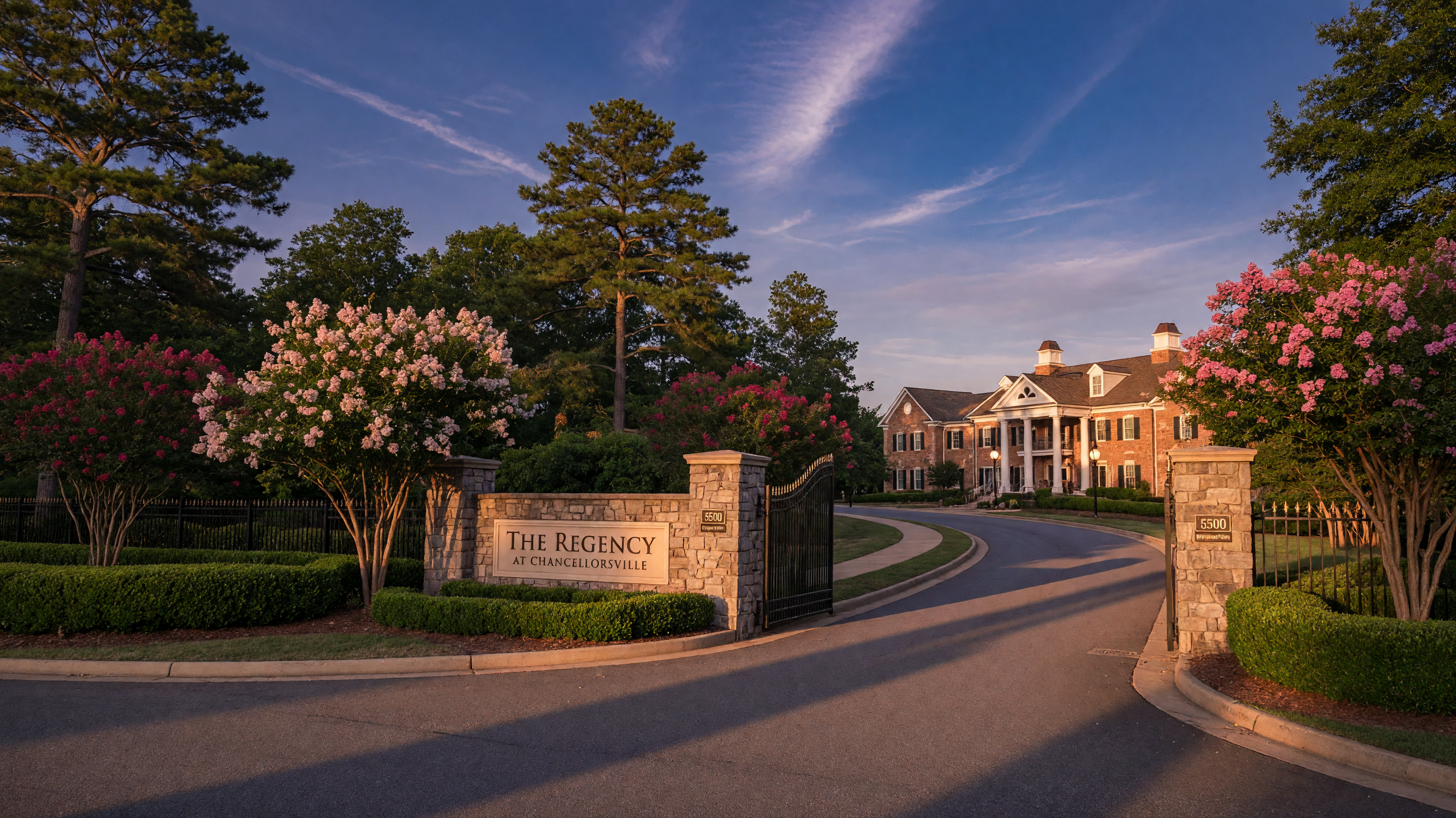 Regency at Chancellorsville gated 55+ active adult community entrance in Spotsylvania County Virginia — stone pillars, manicured landscaping, Toll Brothers community sign, clubhouse visible in the distance, warm golden hour light