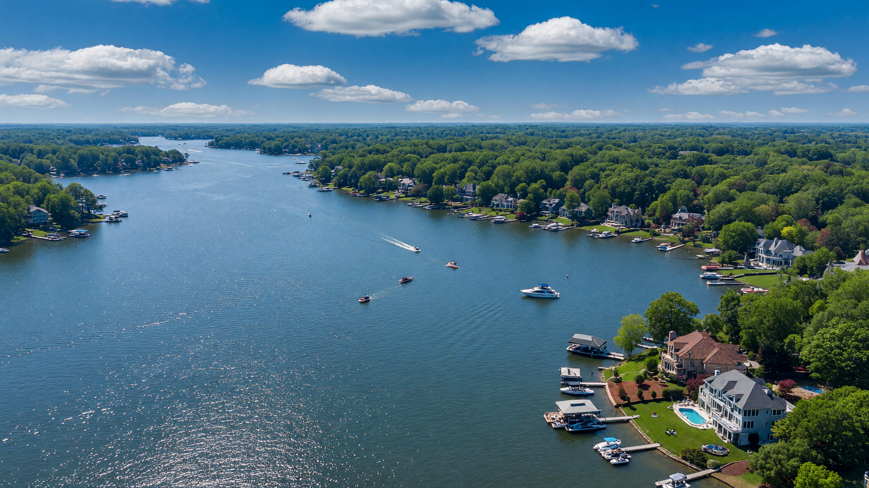 Breathtaking aerial view of Lake Norman North Carolina with luxury waterfront estates, private docks, and boats on the sparkling blue water surrounded by lush forested shoreline