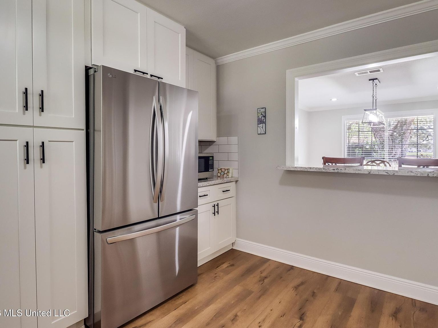Kitchen with white shaker cabinets, stainless steel refrigerator, and wood-look flooring