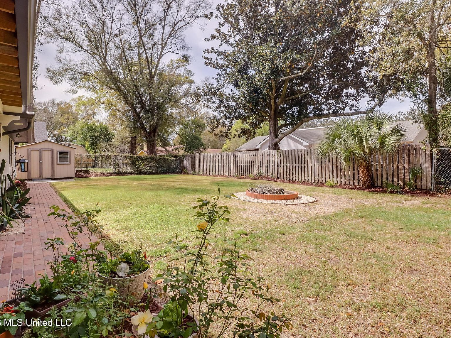 Fenced backyard with grassy lawn, rose bushes, and storage shed