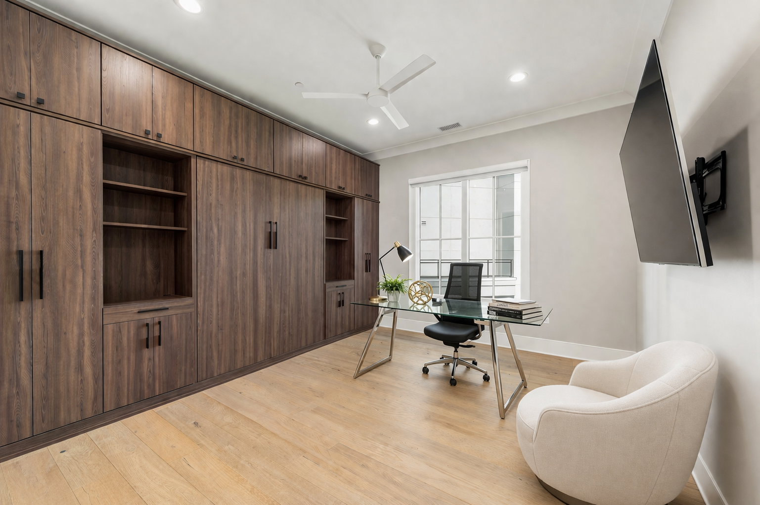 Home office with floor-to-ceiling dark wood built-in cabinetry and glass desk