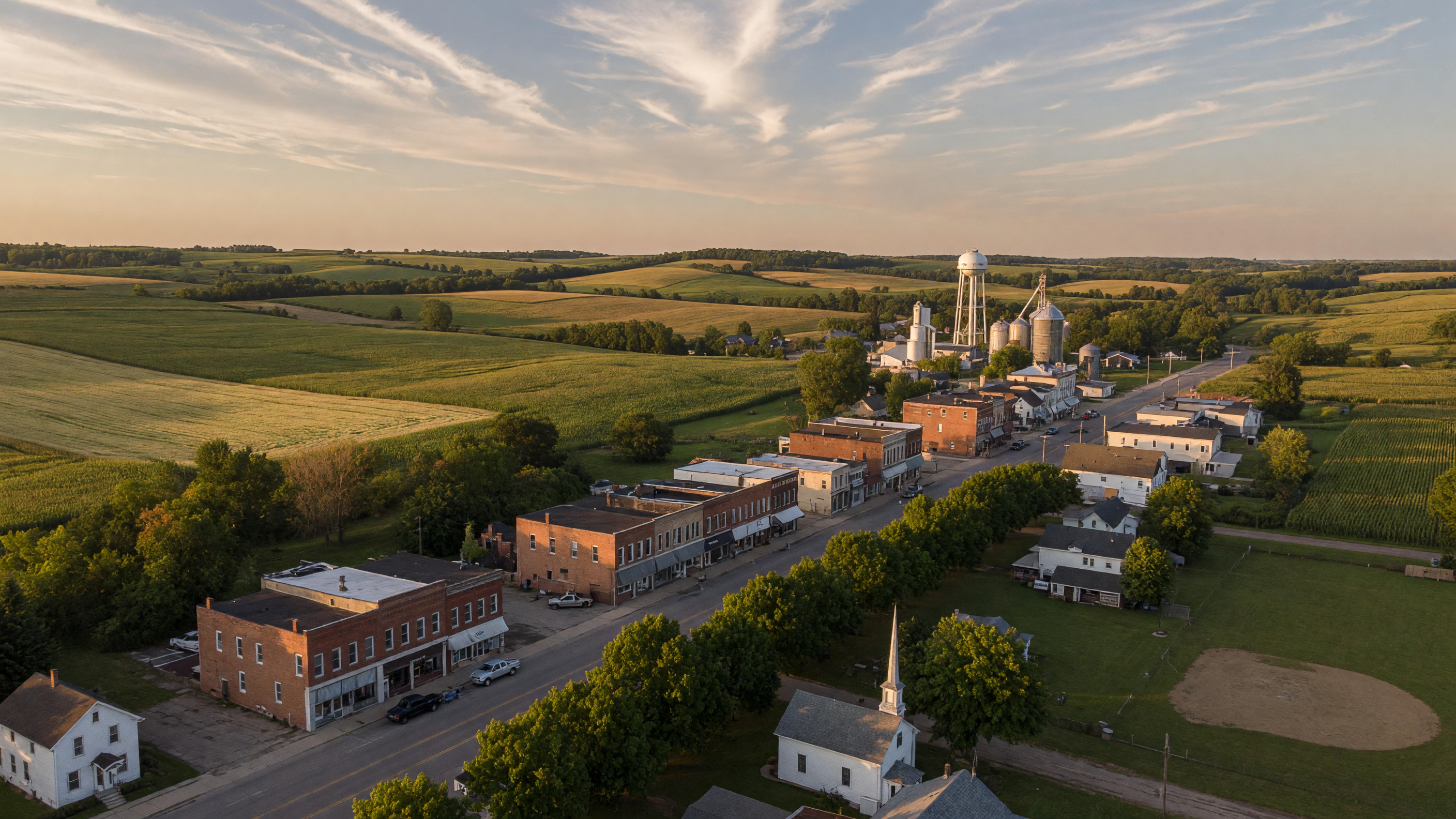 Small-town Main Street in Tuscola County Michigan with historic storefronts, mature trees, and rolling farmland in the distance