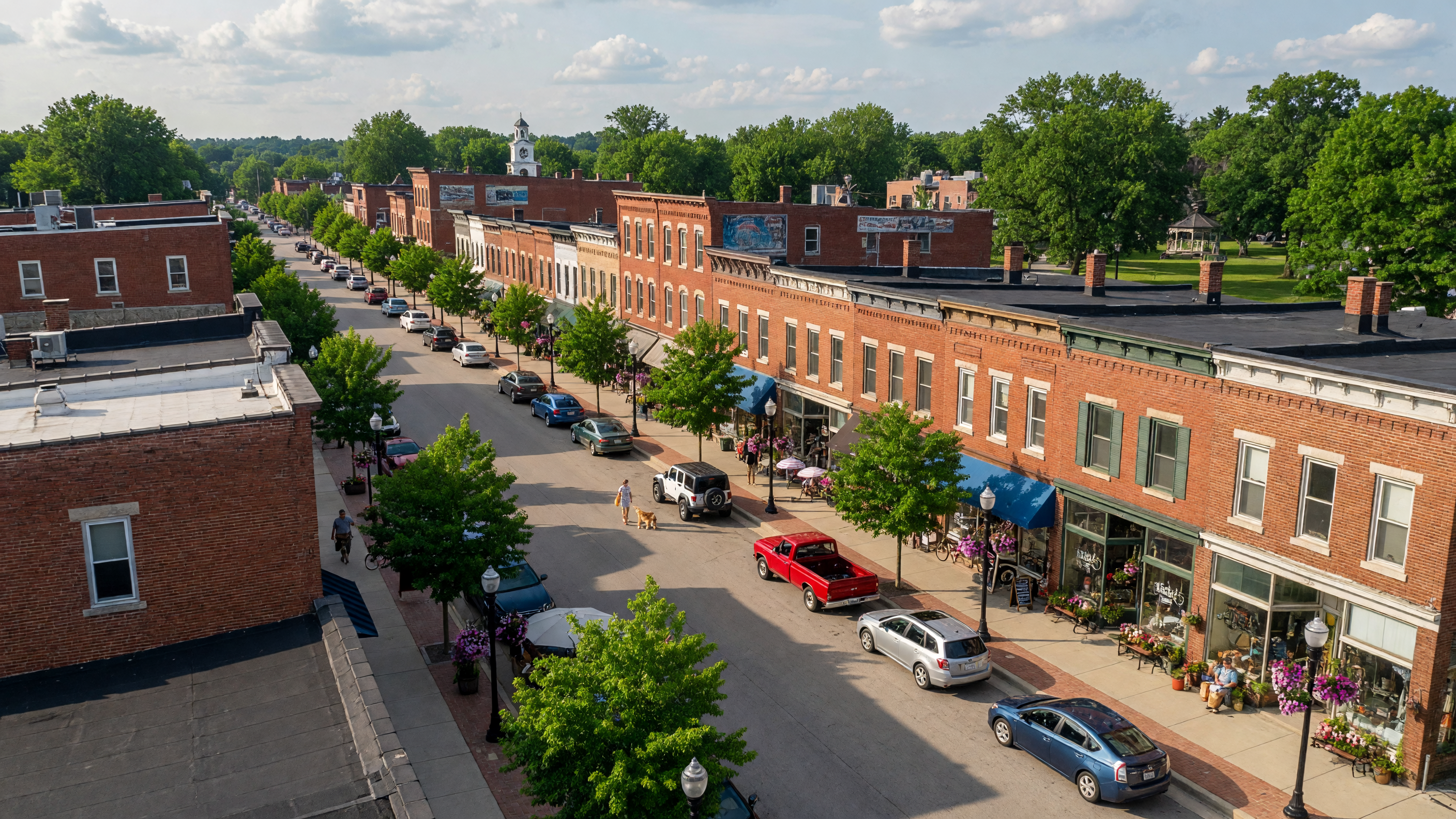 A charming downtown Main Street in Livingston County Michigan with brick storefronts, tree-lined sidewalks, and a warm summer atmosphere