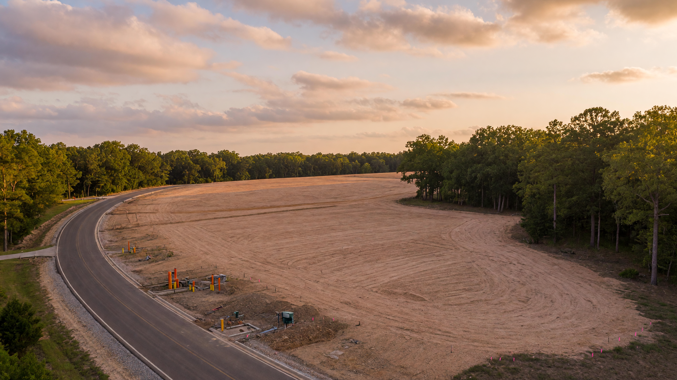 A cleared rural homesite in Northeast Texas with gently rolling land, mature trees along the perimeter, and utility stubs at the road frontage
