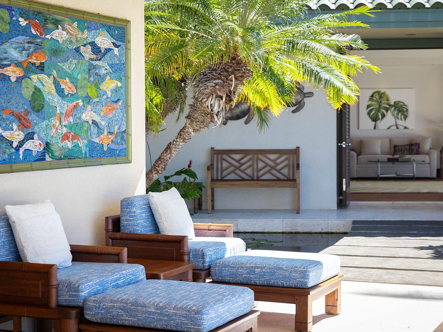 Covered outdoor lanai lounge with blue-cushioned seating, mosaic koi panel, palm trees
