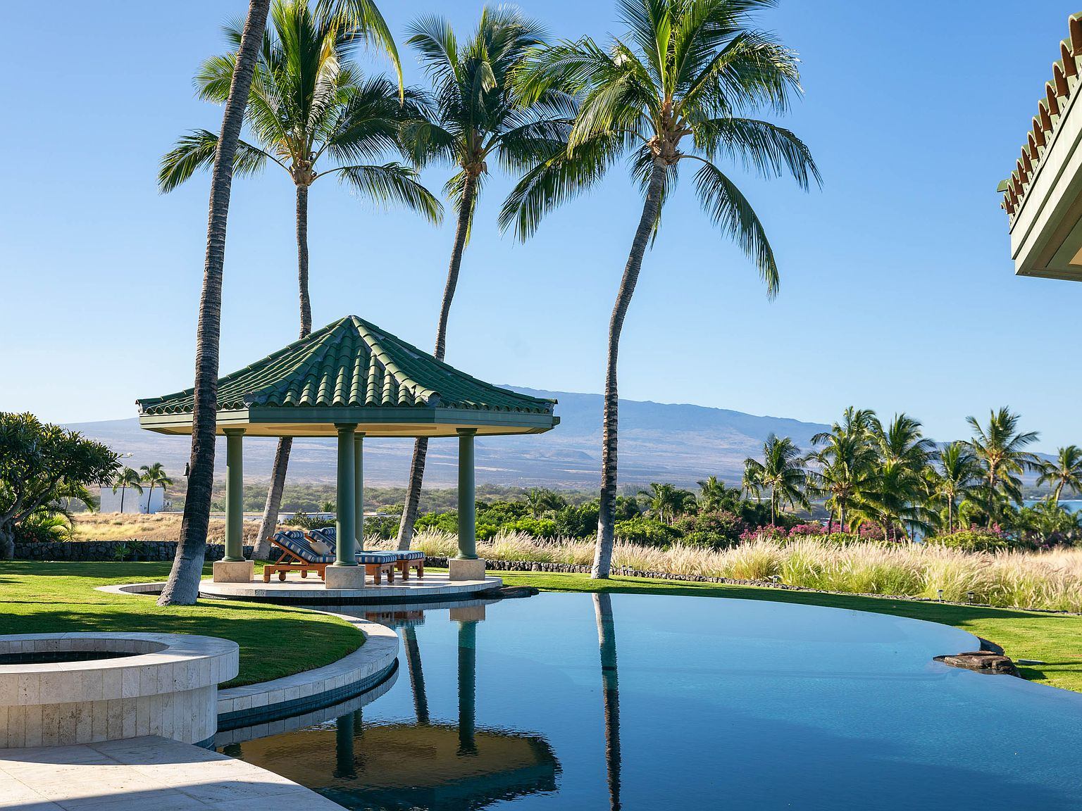 Infinity pool with palm trees, manicured lawns, and pavilion with green tile roof