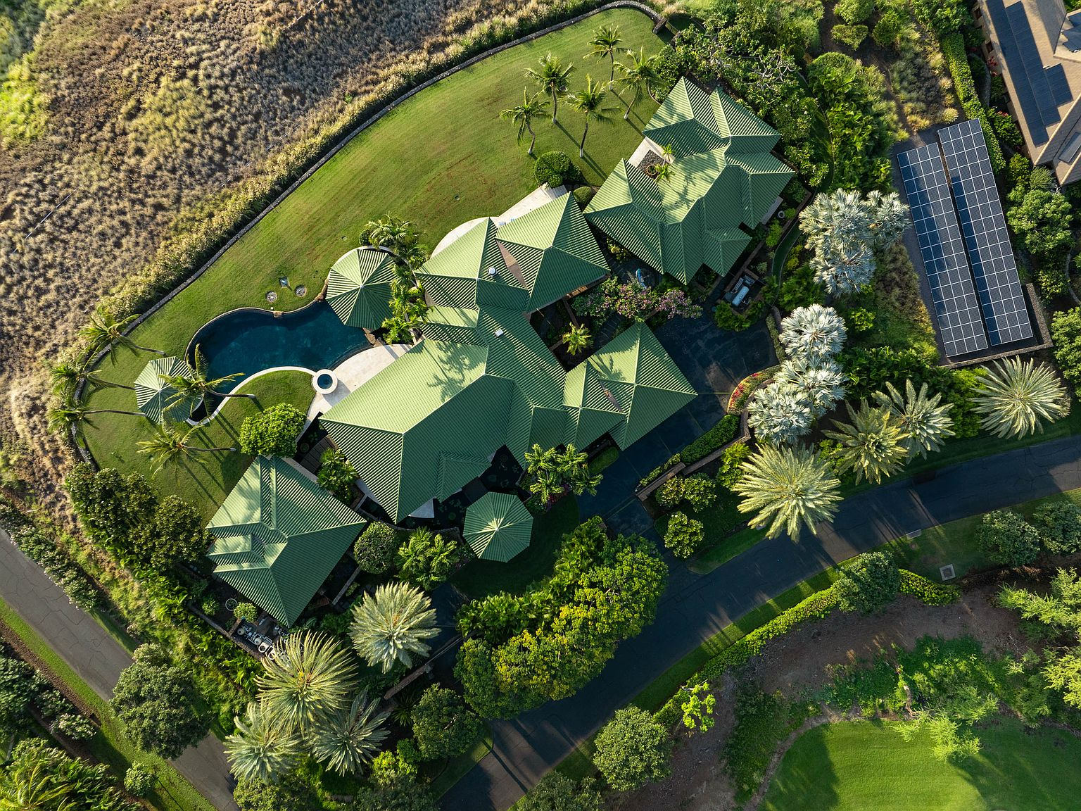 Top-down aerial of estate with green-tiled roofs, manicured lawns, palm trees, and solar panels