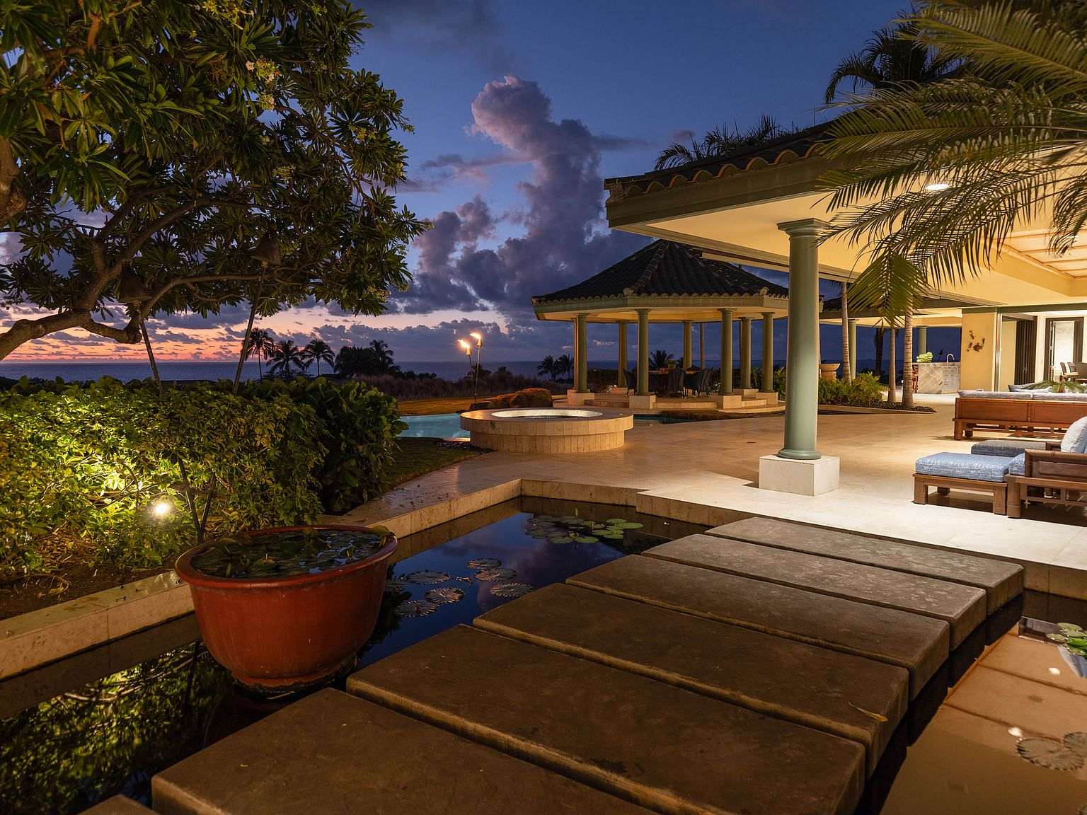 Stepping-stone path over pond toward lanai at twilight with tiki torches and ocean view