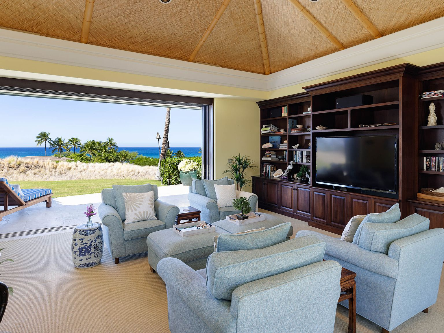 Living room with vaulted bamboo ceiling, dark wood built-in shelving, pocket doors to ocean