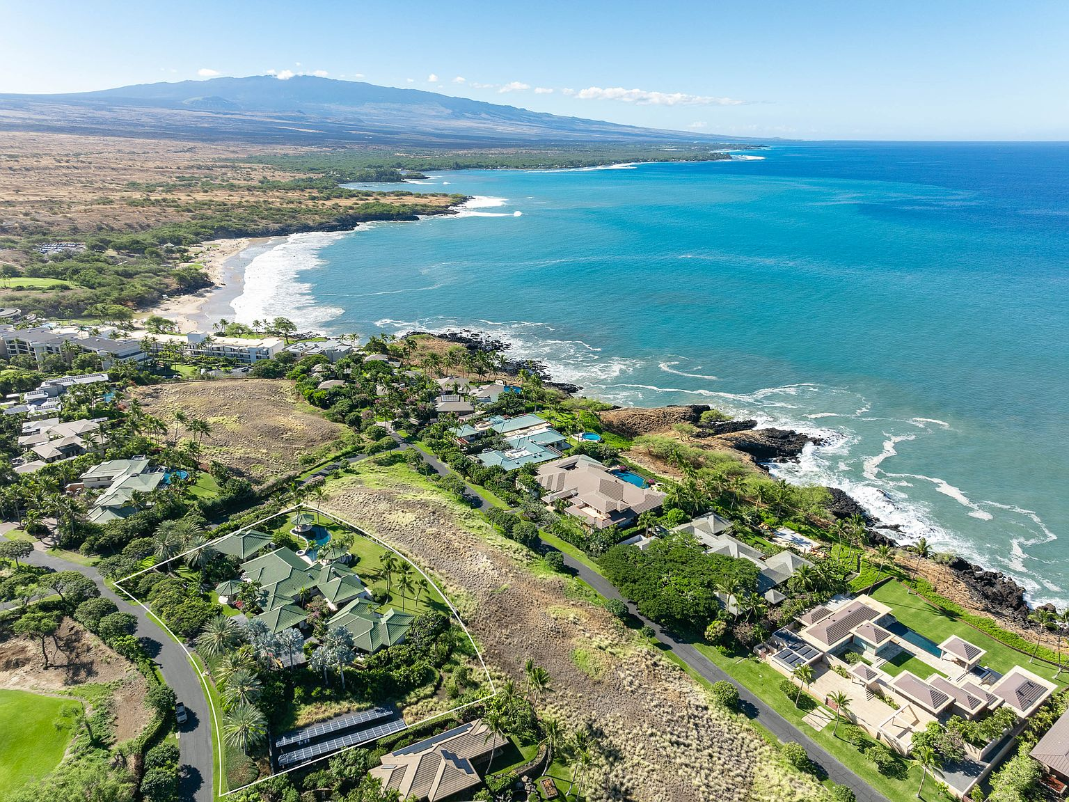 High-altitude aerial of tropical coastline, ocean, and luxury resort estates with green-tiled roofs