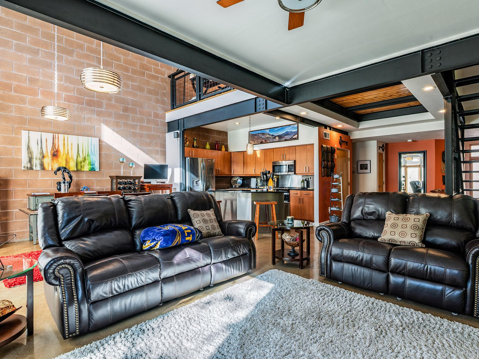 Open-concept living room with steel beams, concrete walls, and upper loft overlook