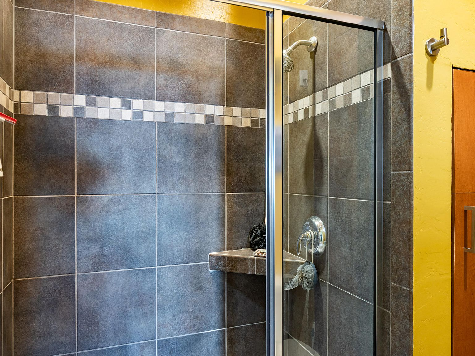 Tiled shower with dark gray wall tiles and mosaic accent