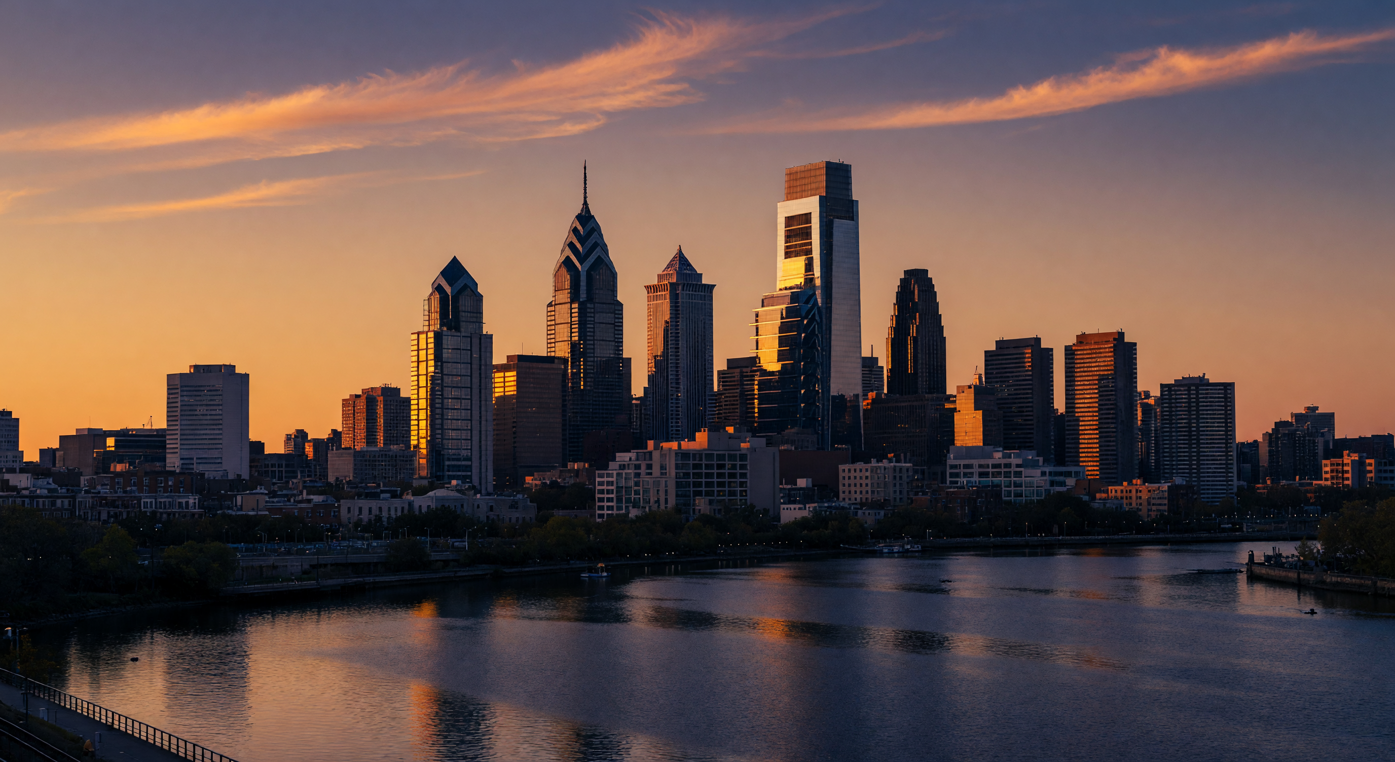 Philadelphia skyline at golden hour with iconic skyscrapers reflecting warm light across the river