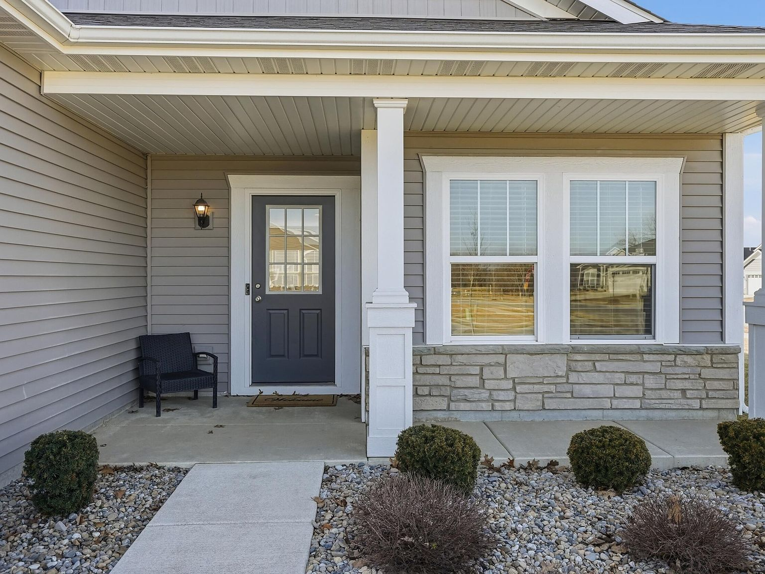 Front porch with white square columns, stone veneer, and dark gray entry door