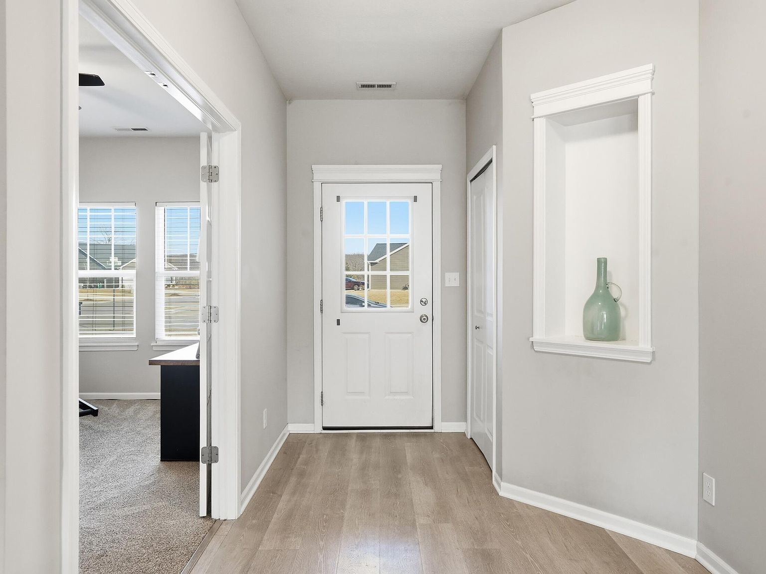 Interior entryway with light wood laminate flooring, neutral gray walls, and a built-in display niche