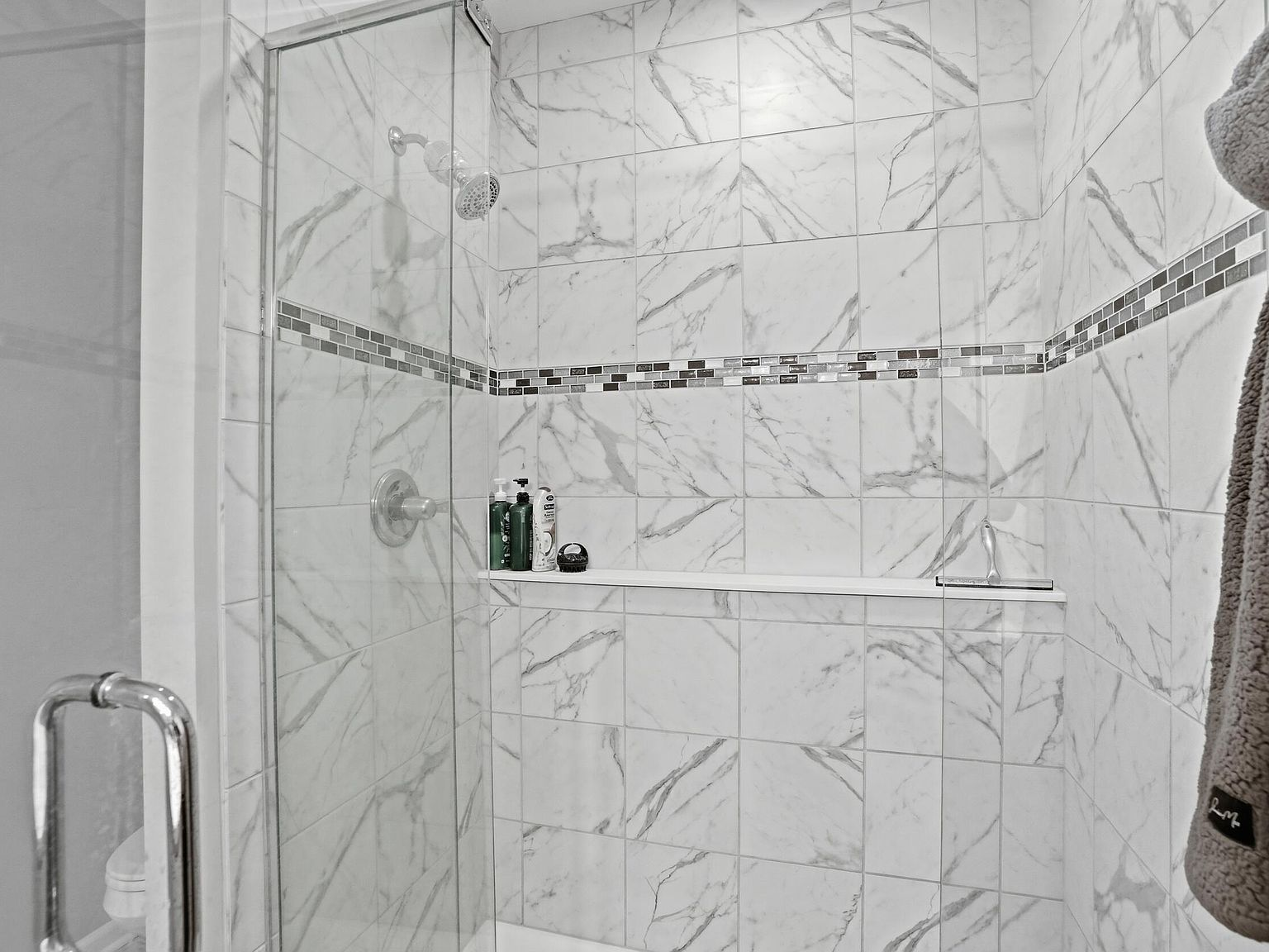 Primary bathroom walk-in shower with marble-pattern tile and glass enclosure
