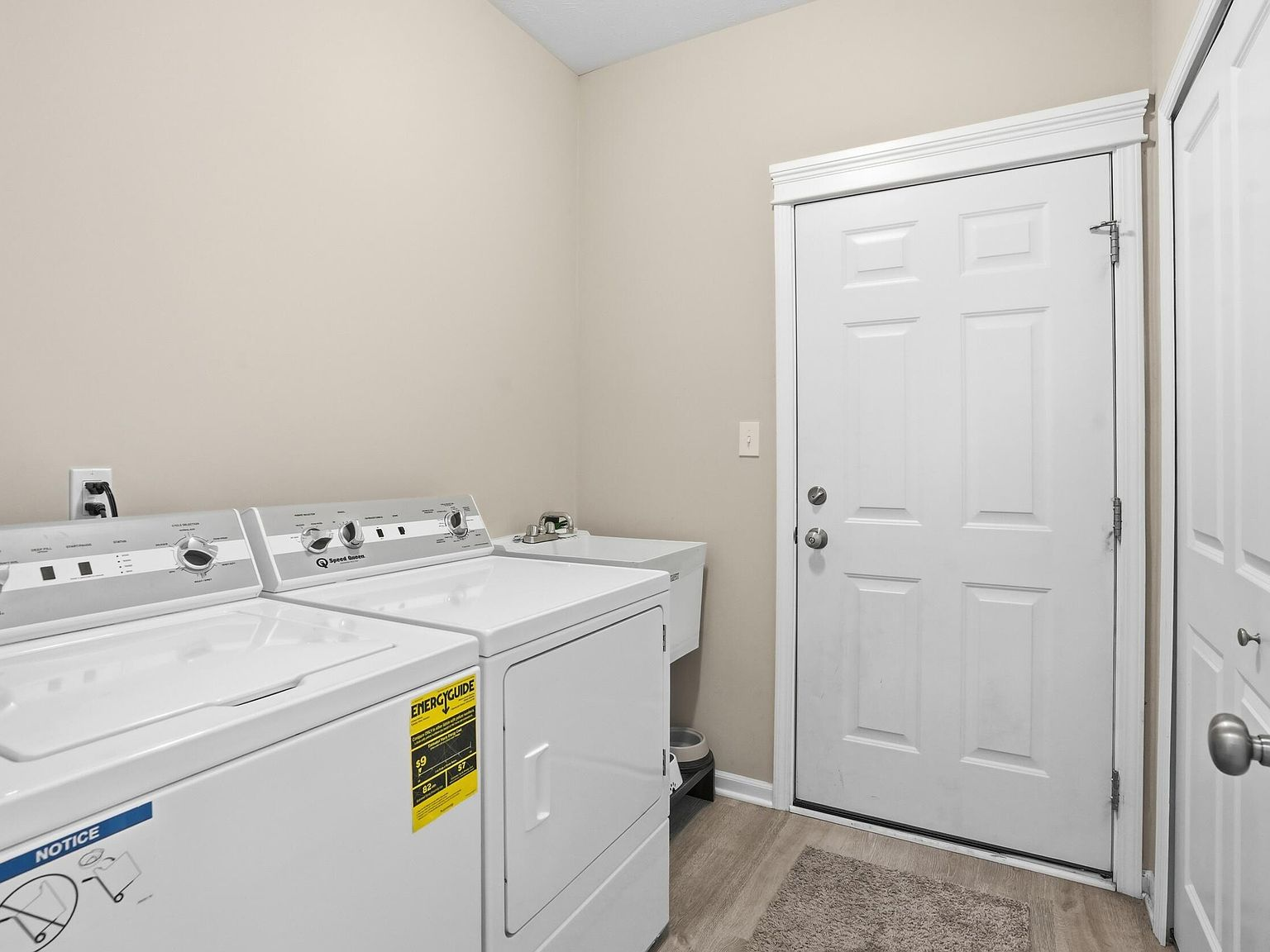 Laundry room with white washer and dryer, utility sink, and wood laminate flooring