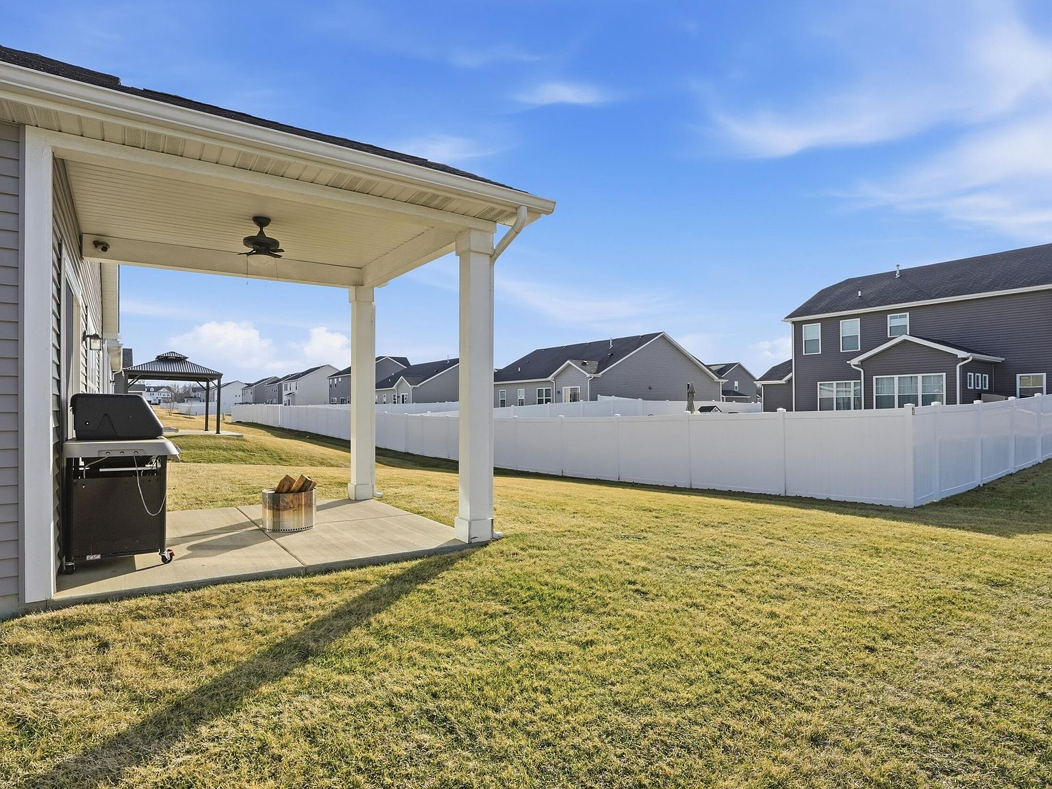 Backyard covered patio with gray vinyl siding, white support pillars, and vinyl privacy fencing