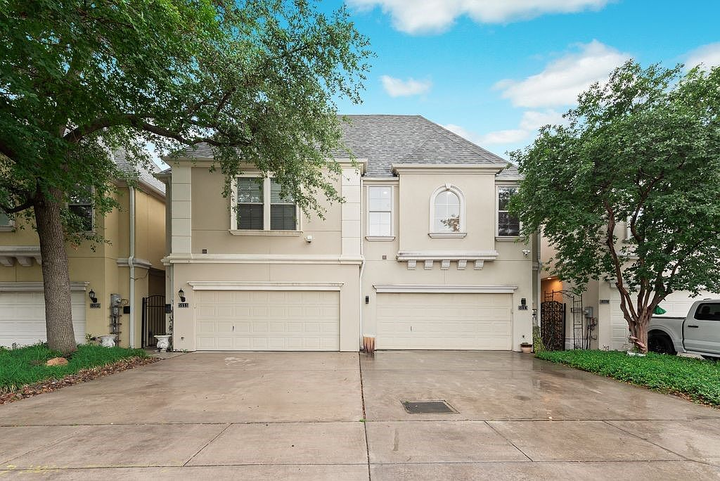 Exterior front shot of the modern townhome at 5113 Vandelia St with beige stucco walls, concrete driveway, and two-car garage under a bright sky
