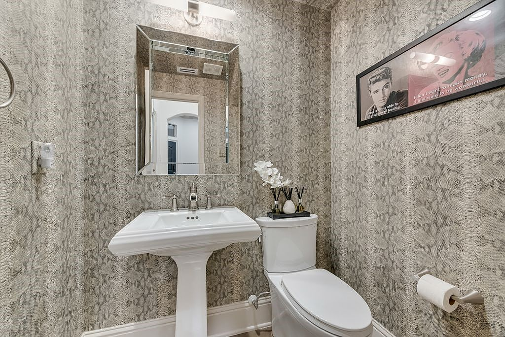 Powder room with textured wallpaper, pedestal sink, and chrome-bordered mirror