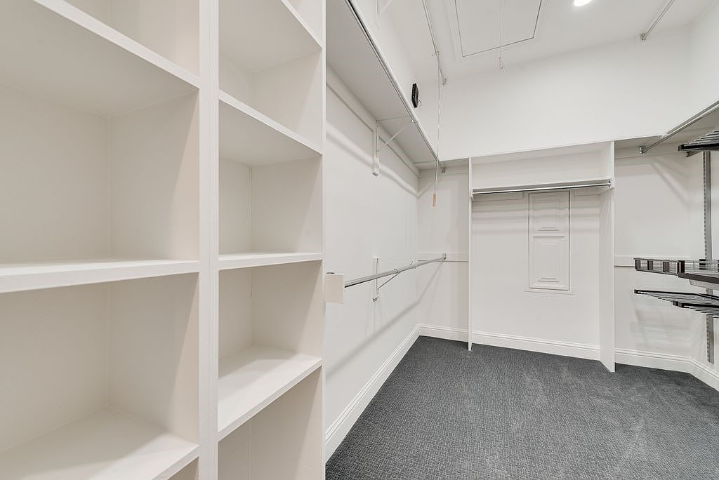 Walk-in closet with custom white built-in shelving and dark grey carpet