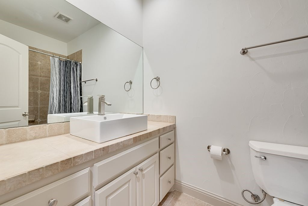 Guest bathroom with vessel sink, beige tile countertop, and white cabinetry