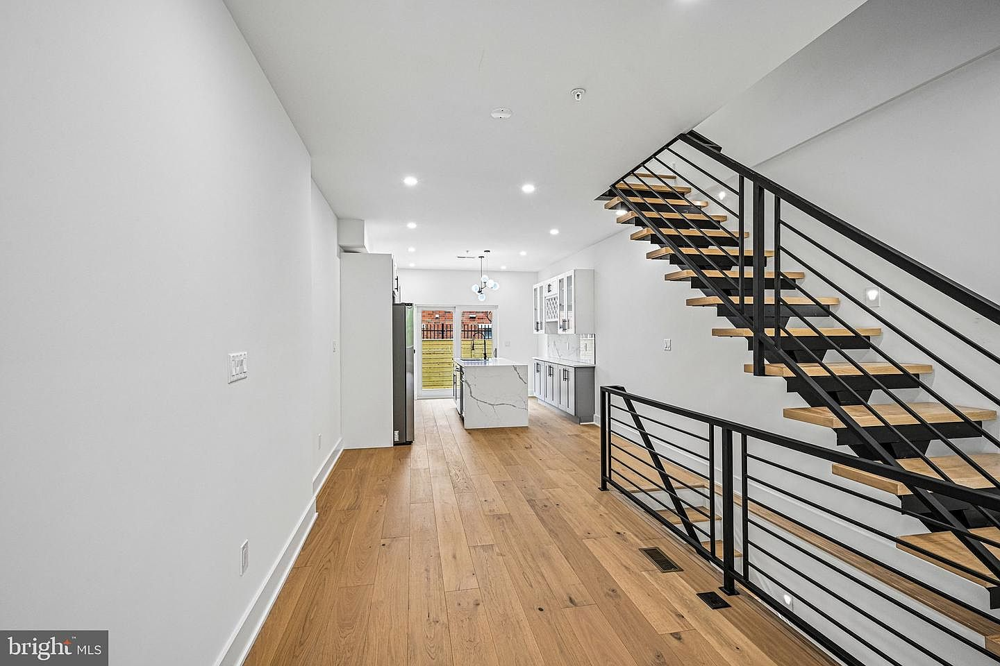 Bright open-concept main floor looking towards custom kitchen with view of floating oak stairs