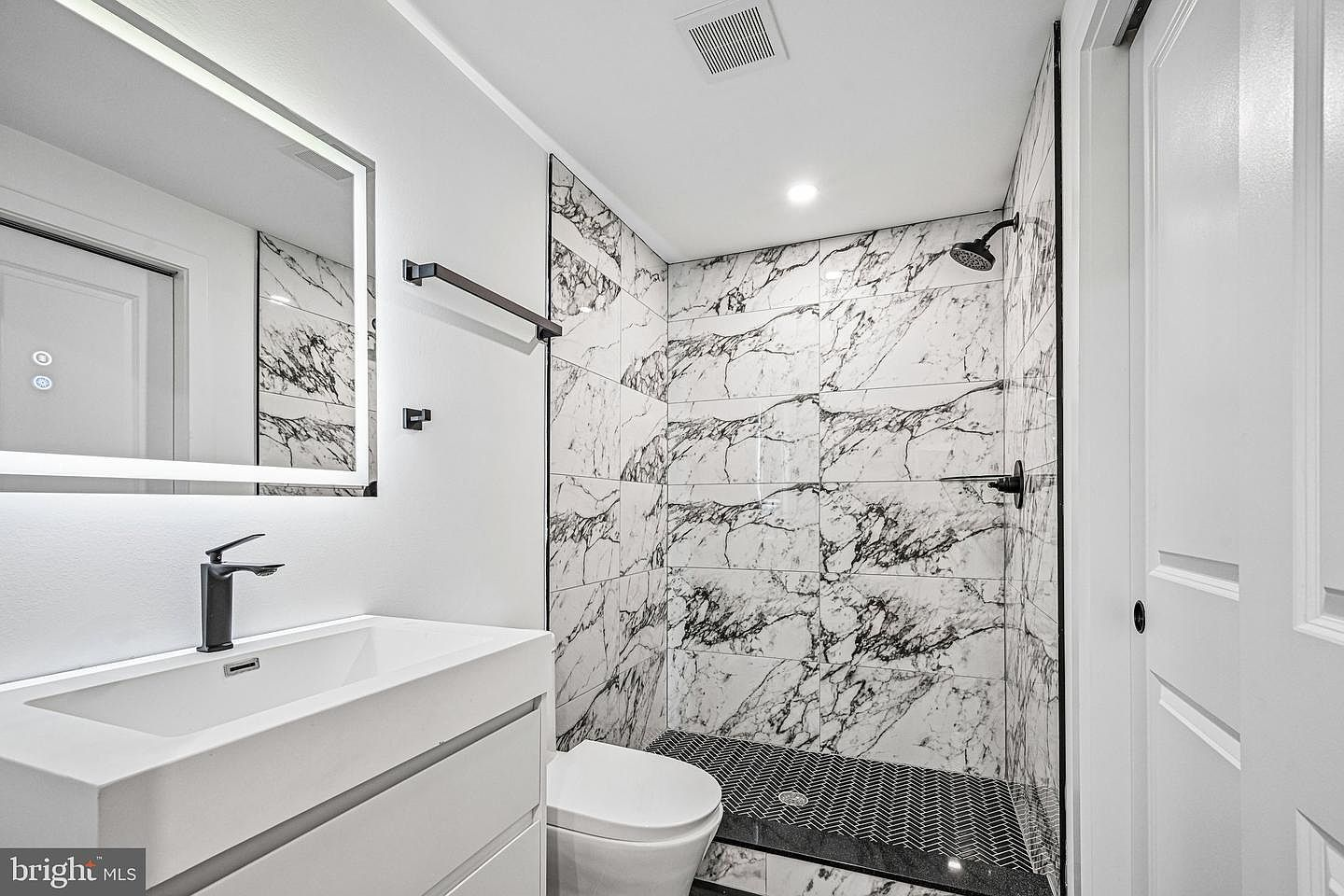 Spa-style bathroom with double white floating vanity, matte black fixtures, and custom marble tile work
