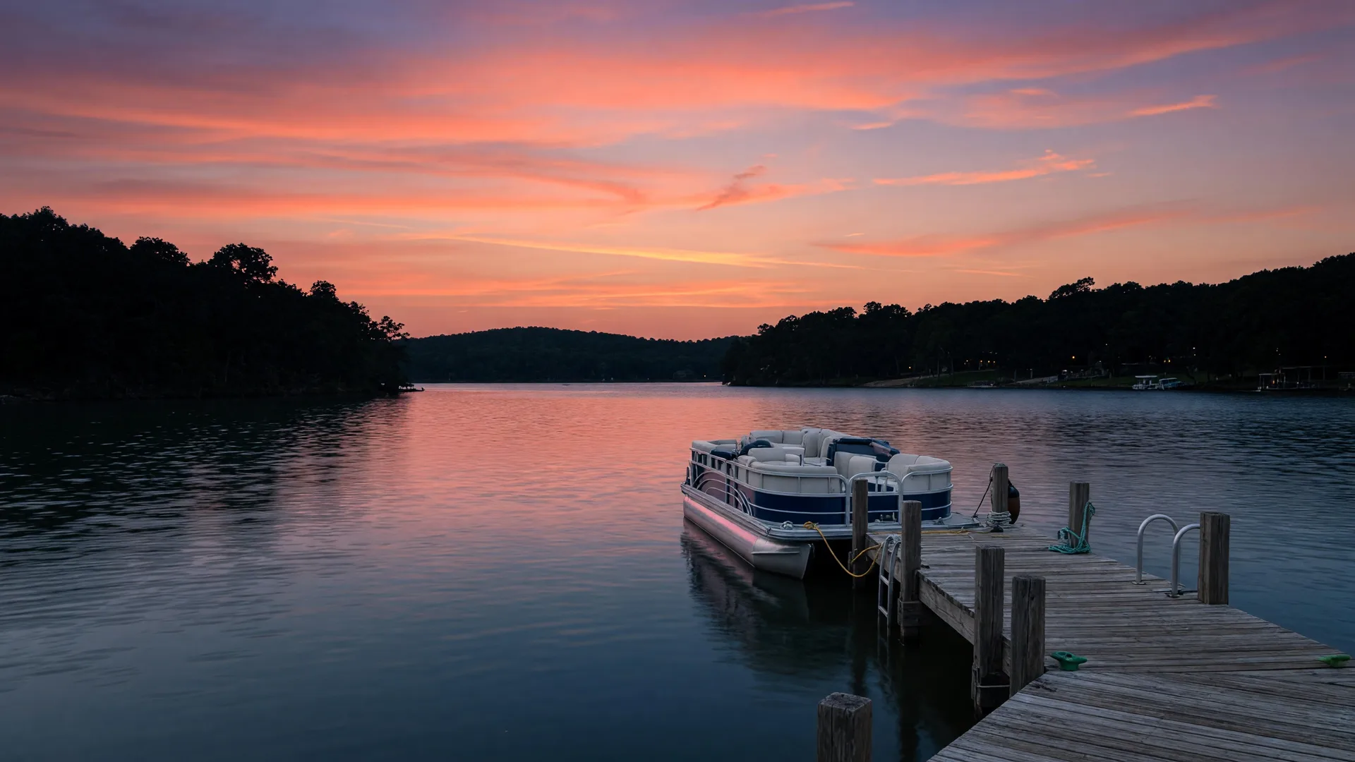 Lake Lewisville at dusk viewed from a wooden dock with a pontoon boat and vibrant sunset sky