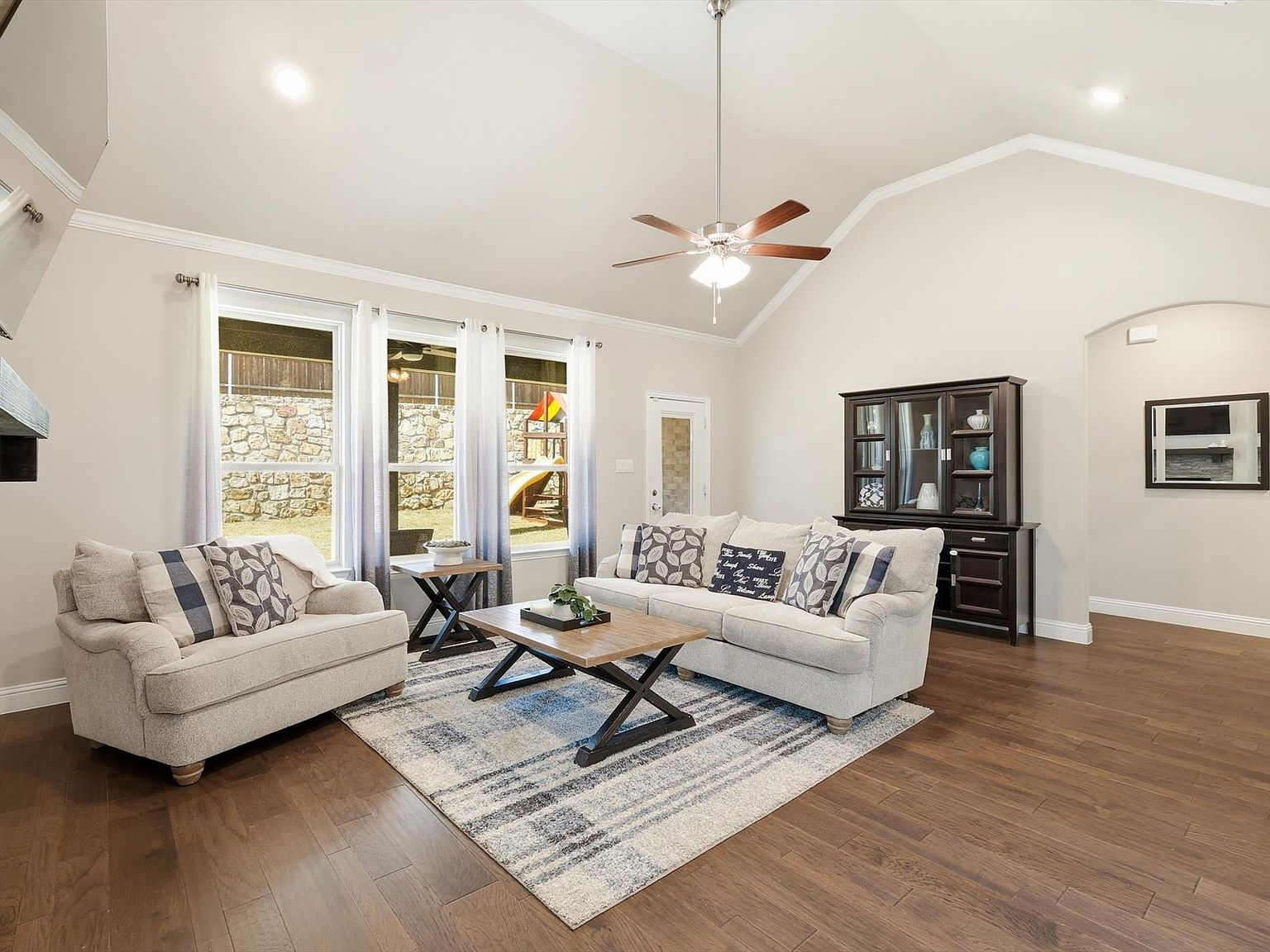 Living room with vaulted ceiling, hardwood floors, and large windows