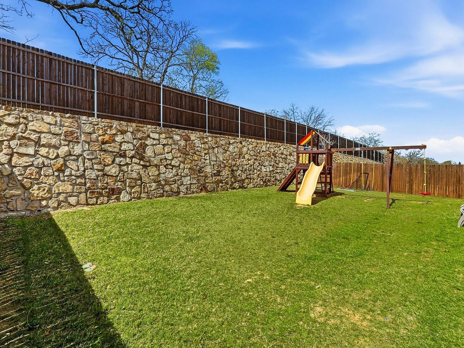 Backyard with stone retaining wall, wooden fence, and green lawn