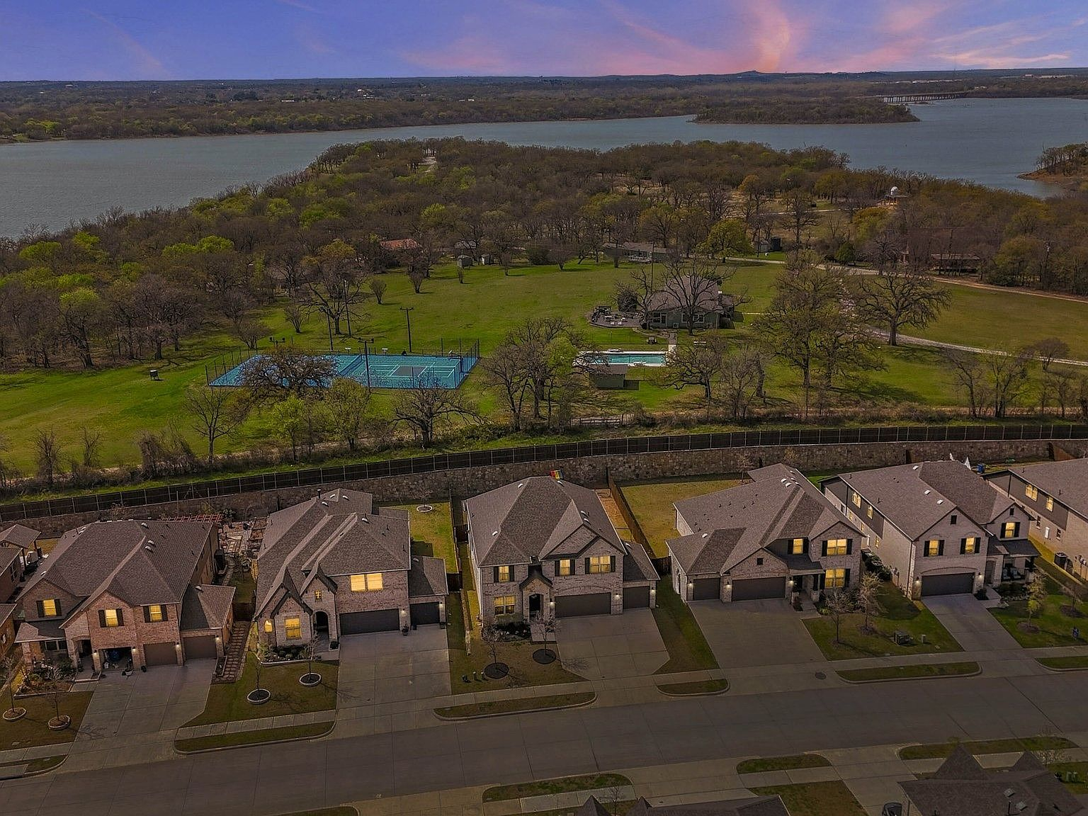 Aerial drone view of Hickory Creek homes at sunset with lake and green trees in the background