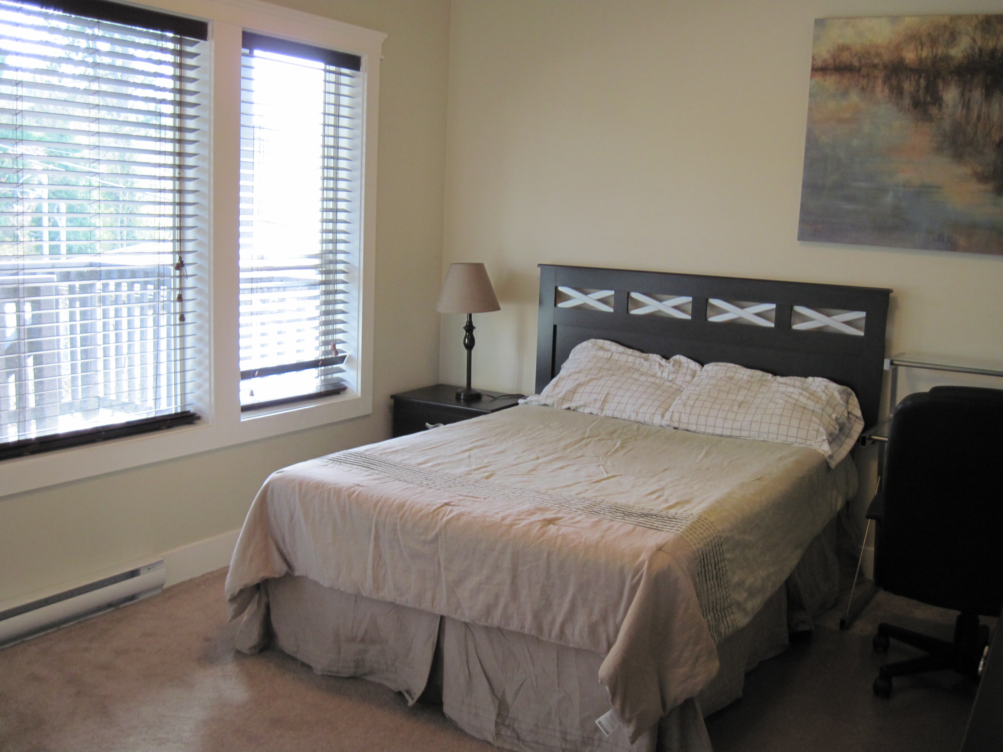 Bedroom with queen bed, dark wood nightstand, and desk workspace by window