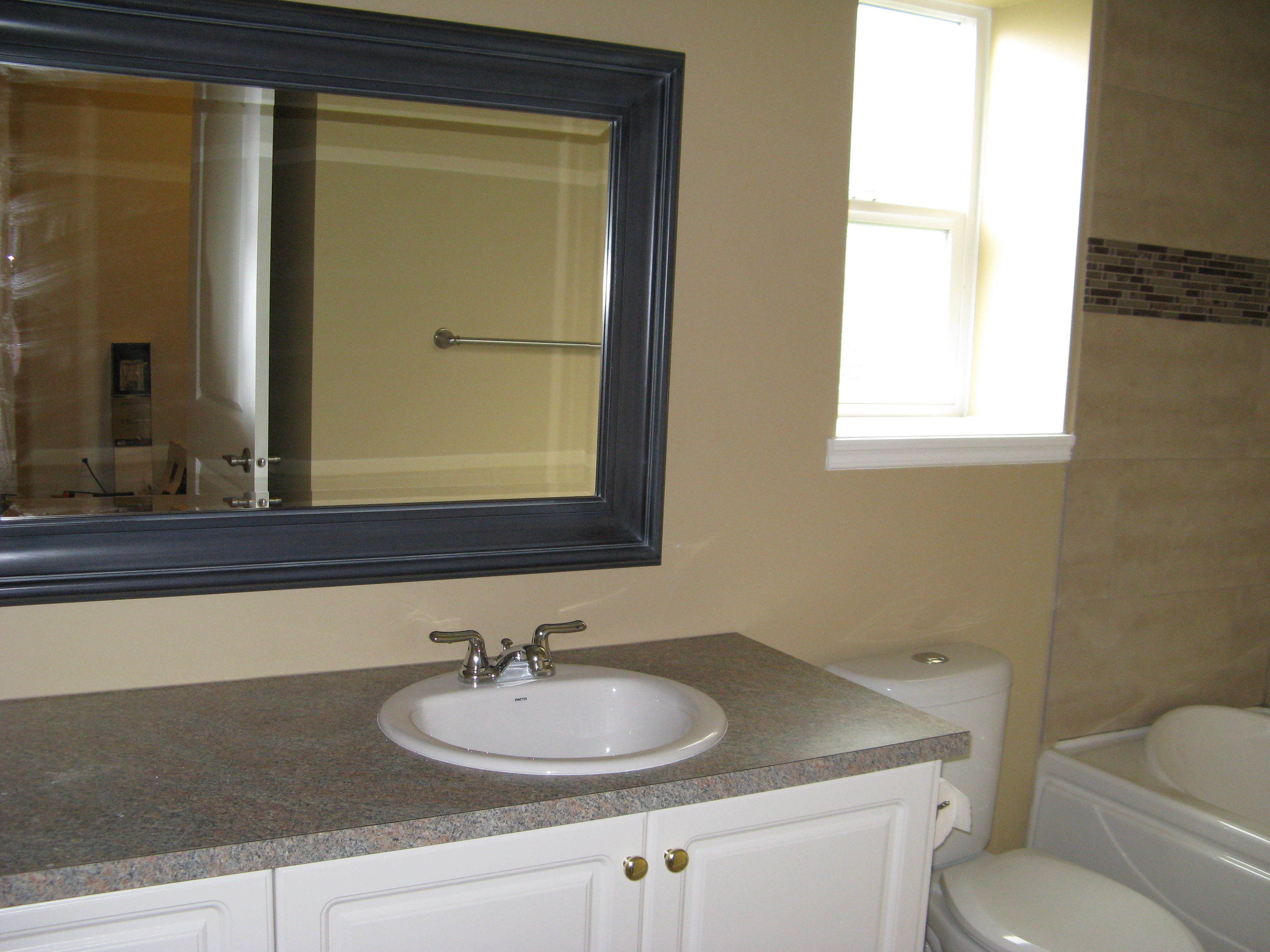 Bathroom vanity with white cabinetry, brass knobs, and large black-framed mirror