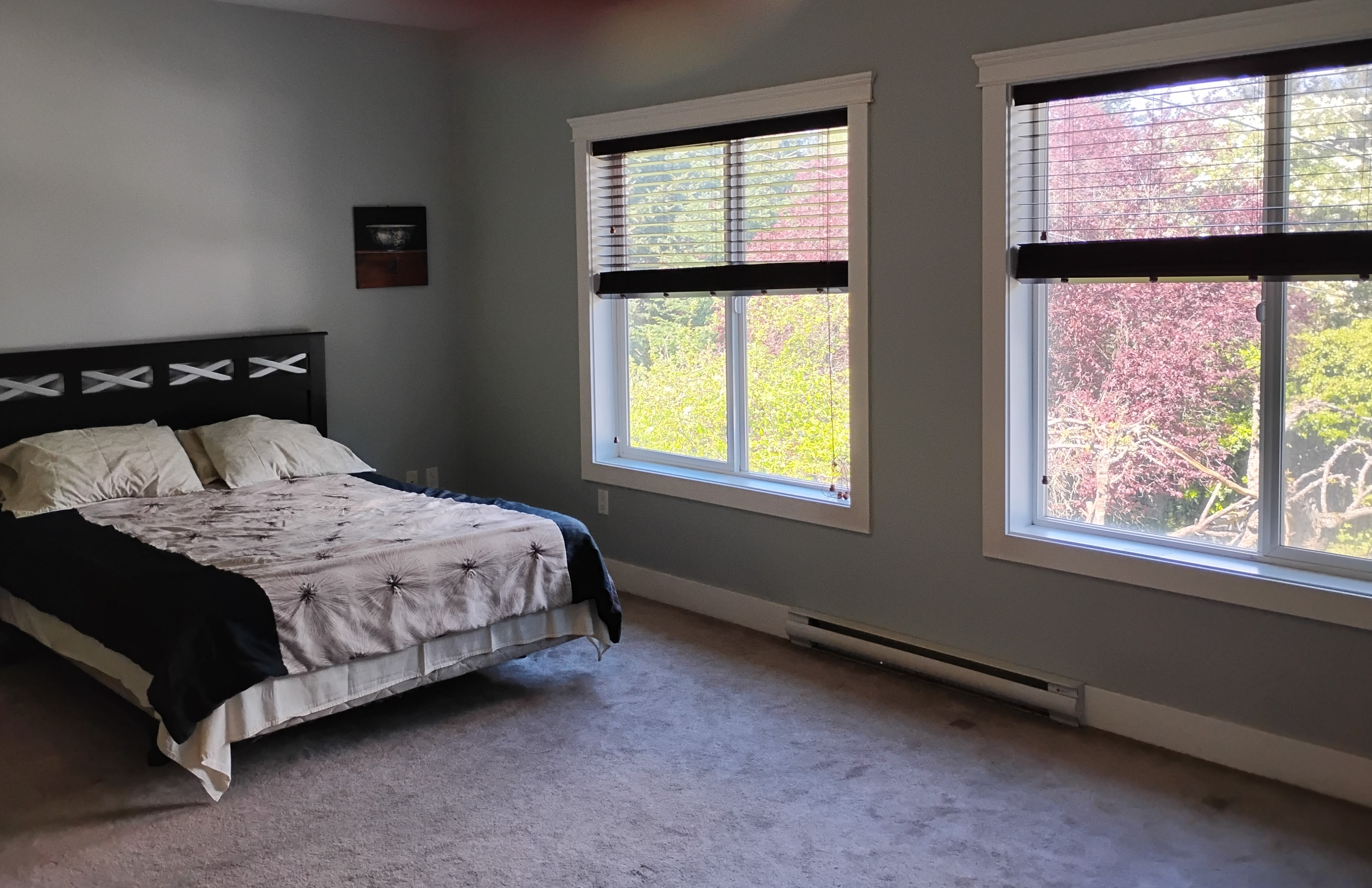 Master bedroom with two large windows showing outdoor trees